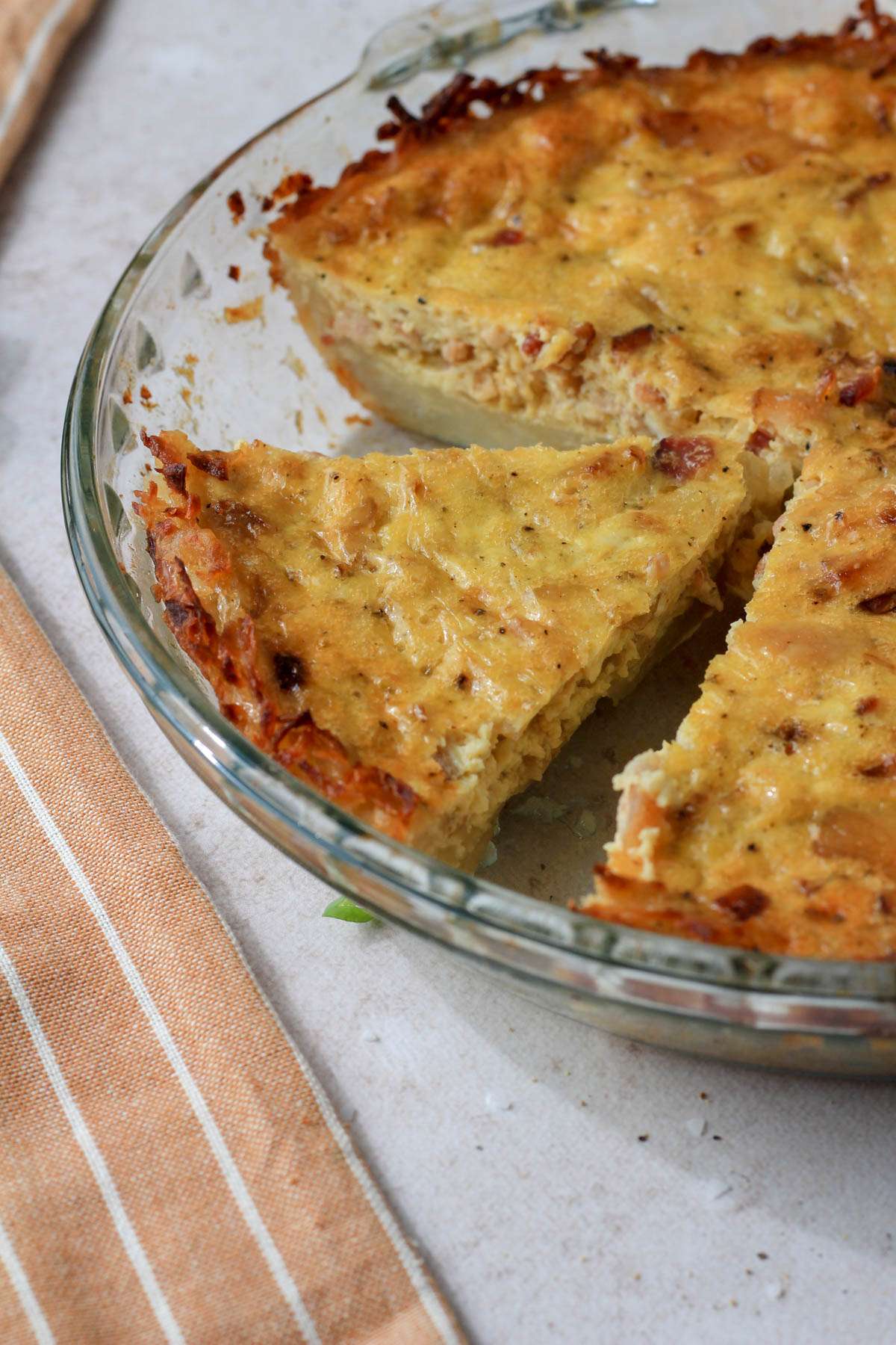 A glass pie dish with a hash brown crusted quiche slice set apart from the rest of the quiche.