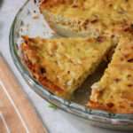 A close up of a slice of dairy-free hash brown crusted quiche in a glass pie dish.