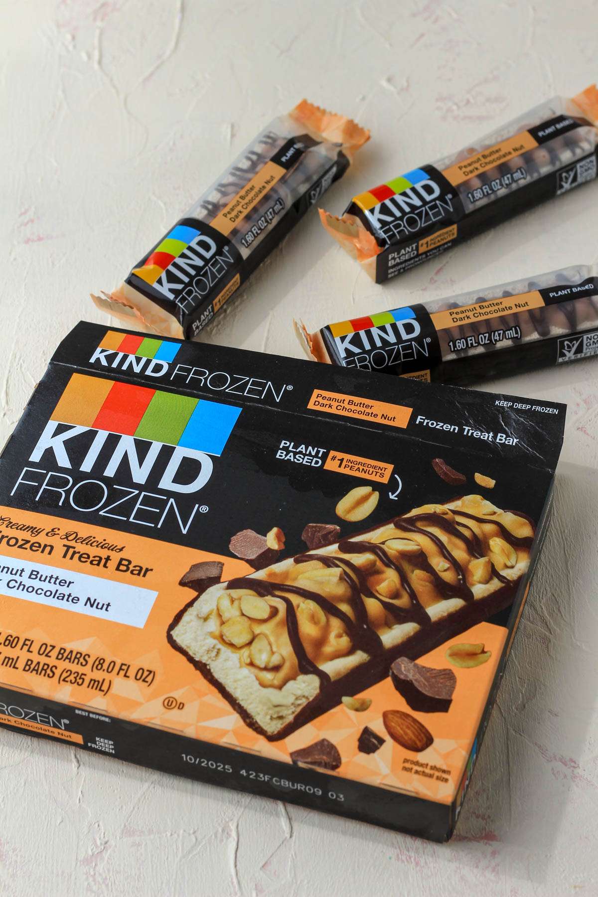 An open orange Kind Frozen peanut butter bars box with three bars on the cream counter.