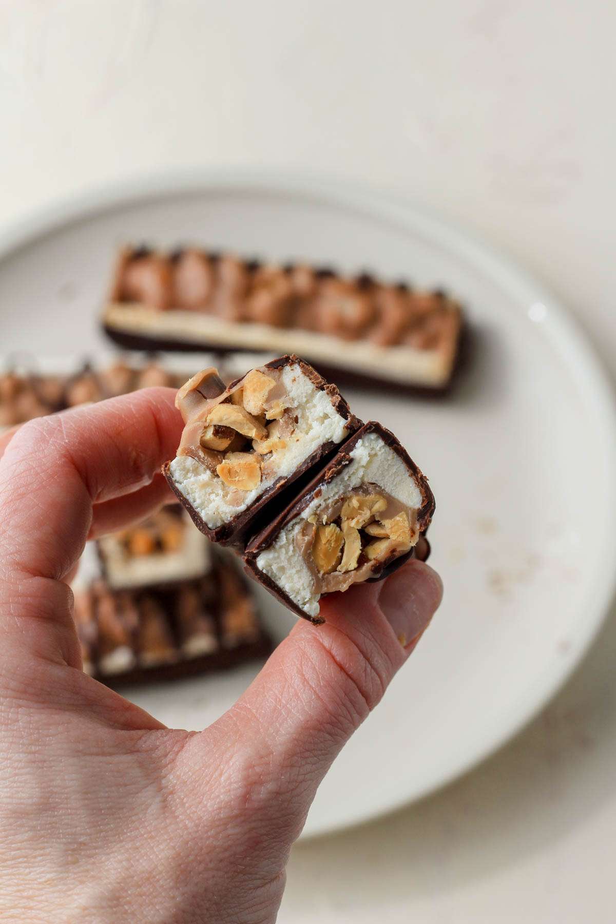 A hand holding a kind frozen almond bar that has been cut in half to show the fillings.