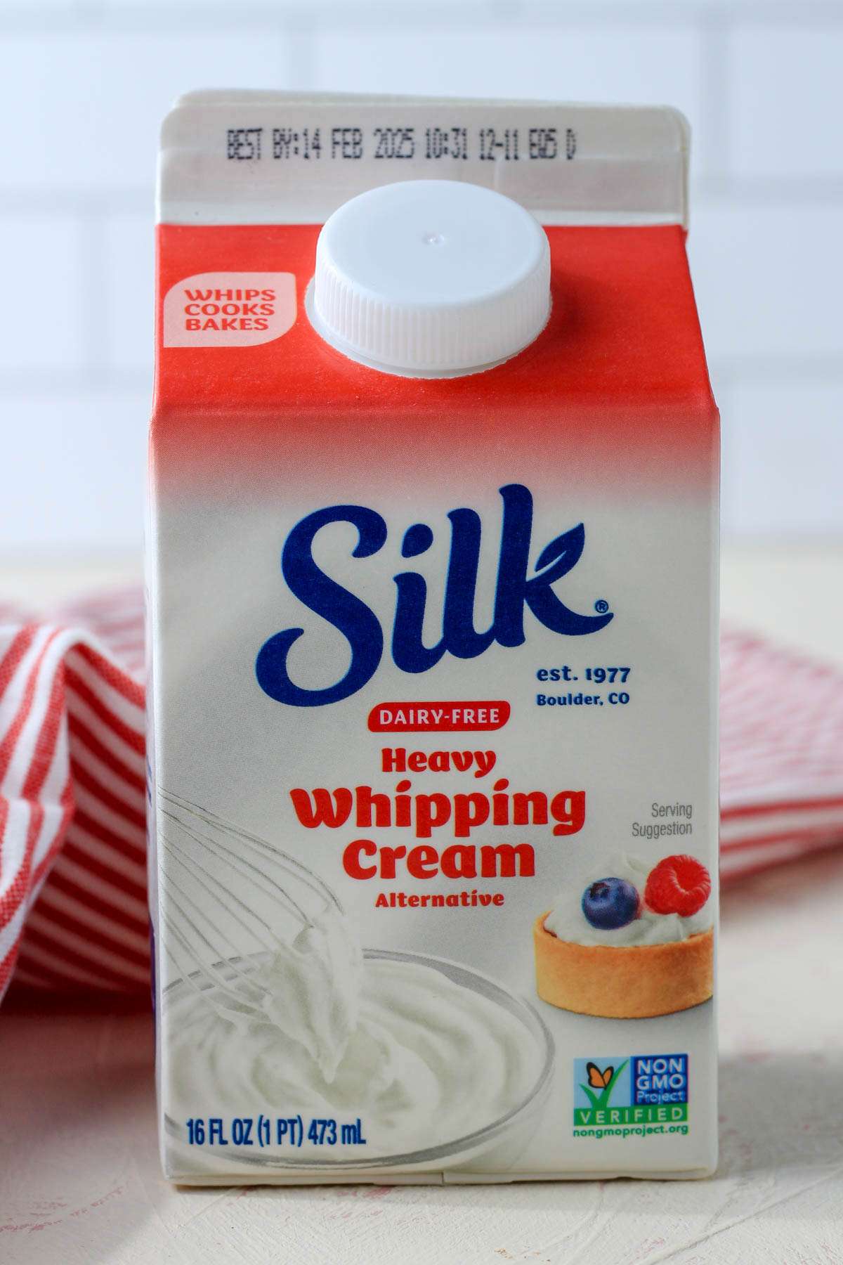 An upright carton of silk dairy-free heavy whipping cream on a cream and pink counter with a red and white towel in the back.
