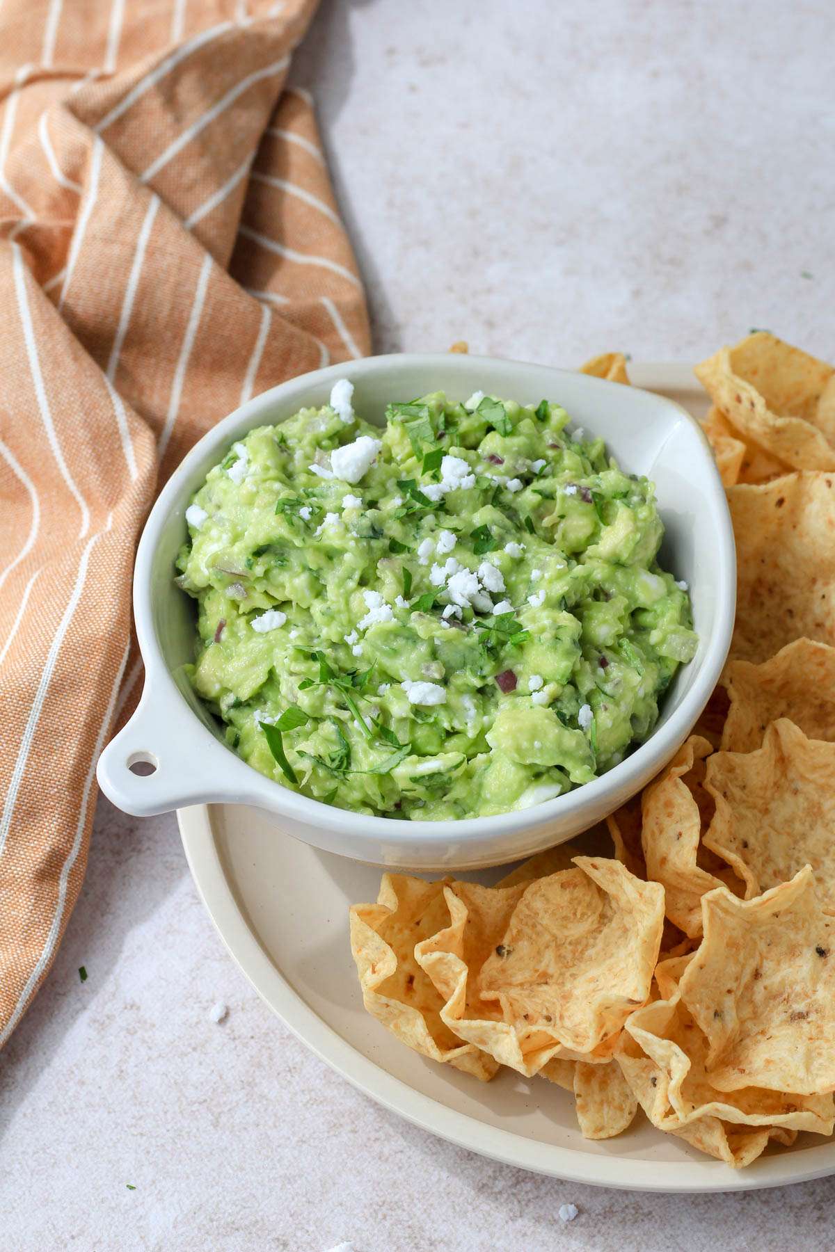 A cream plate with tortilla scoops on the right and a small bowl of avocado and feta dip on the right.