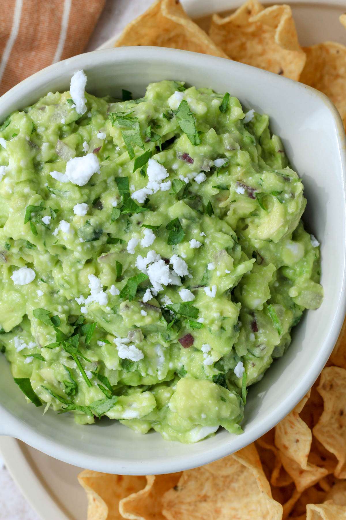 A top down image of vegan feta avocado dip in a cream bowl topped with crumbled feta.
