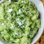 A cropped in image of a cream bowl with vegan feta and avocado dip topped with crumbled vegan feta.