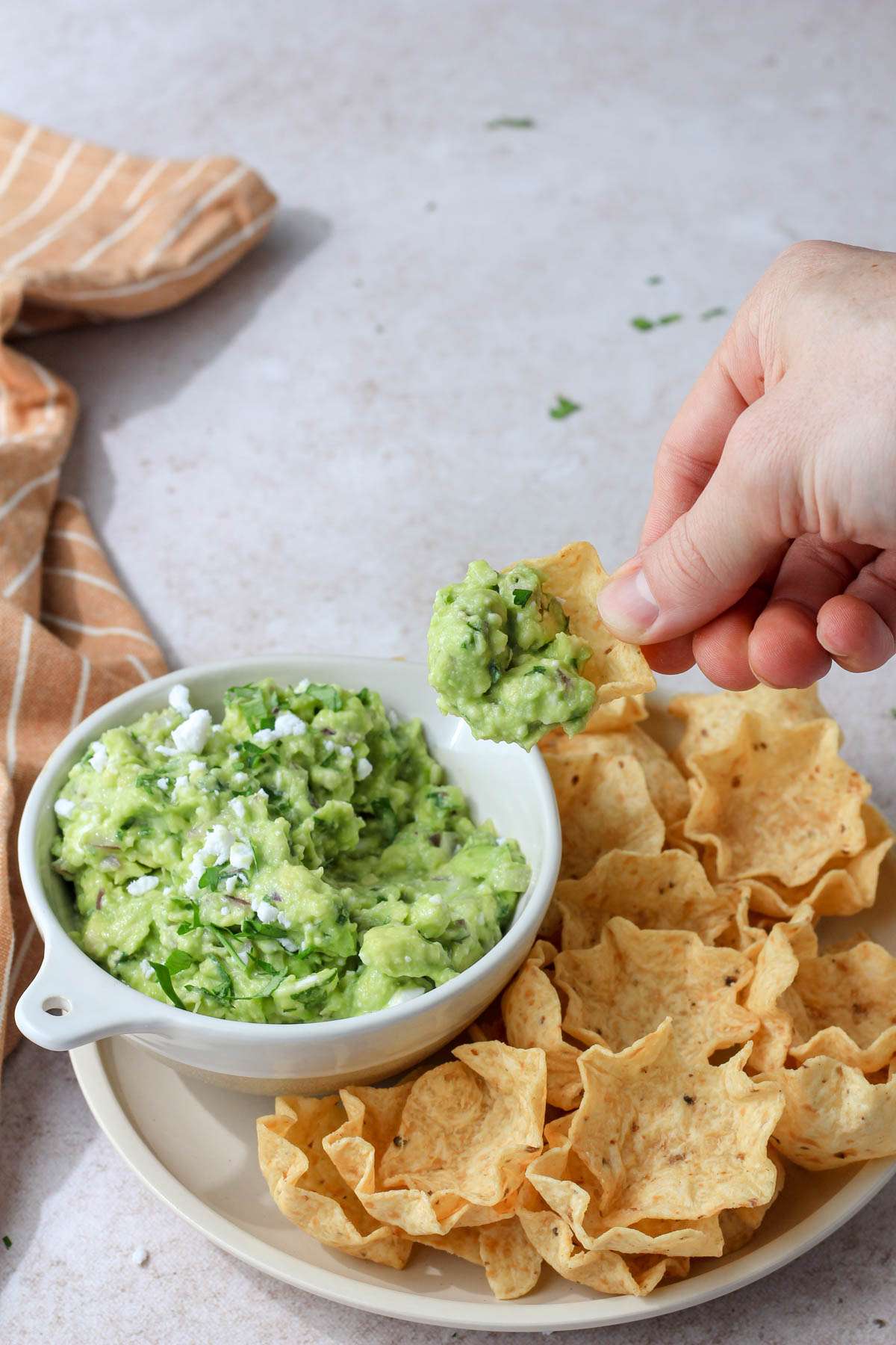 A hand holding a scoop of vegan feta avocado dip over a bowl of avocado dip.
