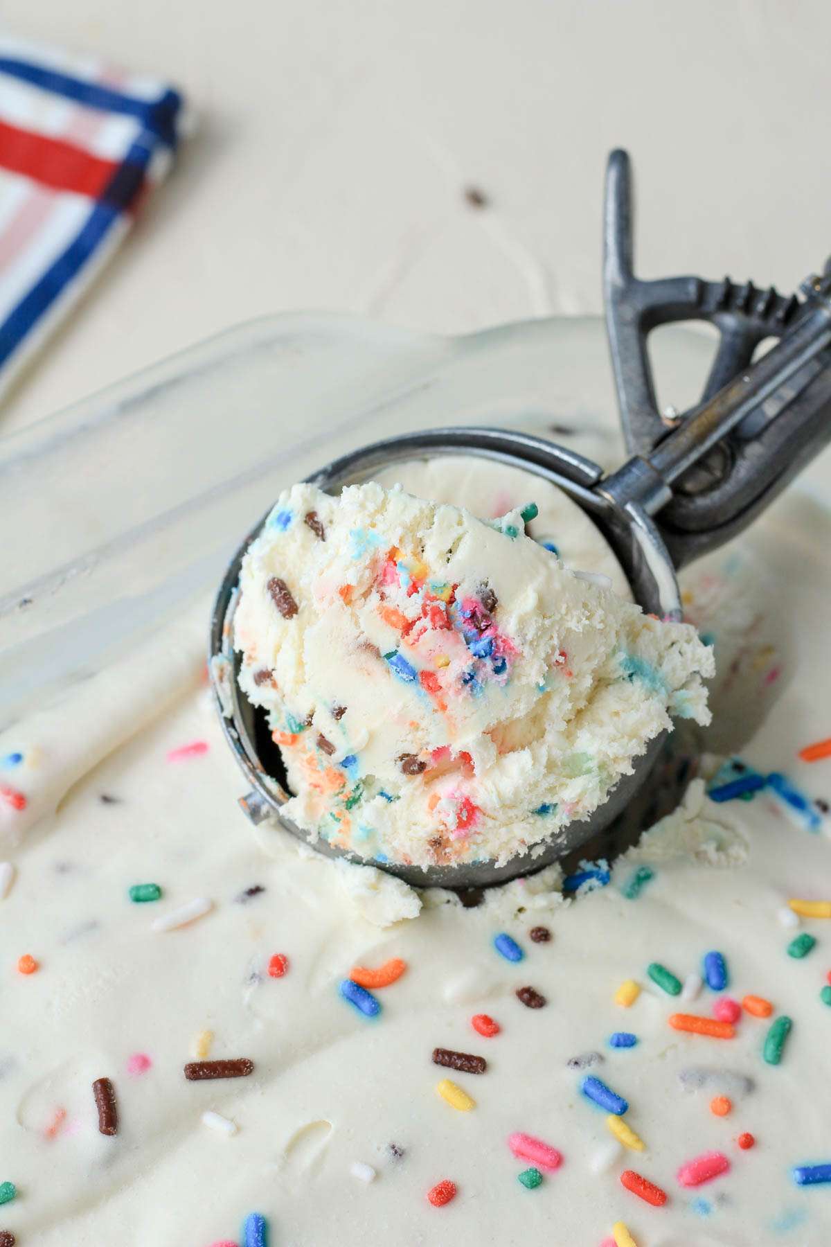 A silver ice cream scoop with a scoop of no churn cake batter flavored ice cream.