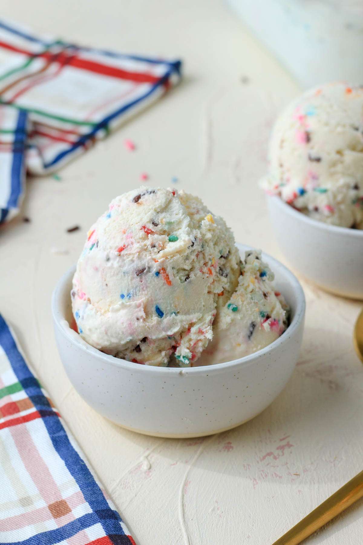 A small white bowl filled with scoops of cake batter ice cream on a cream counter.