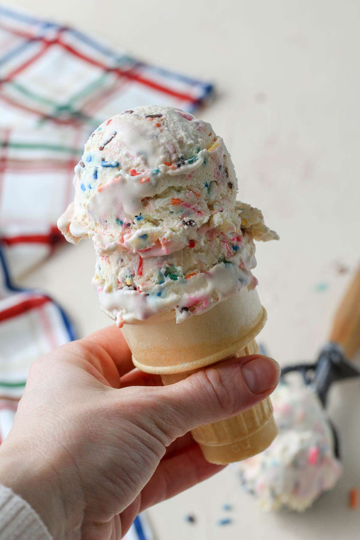 A hand holding a cake cone with two scoops of vegan no churn cake batter flavored ice cream.