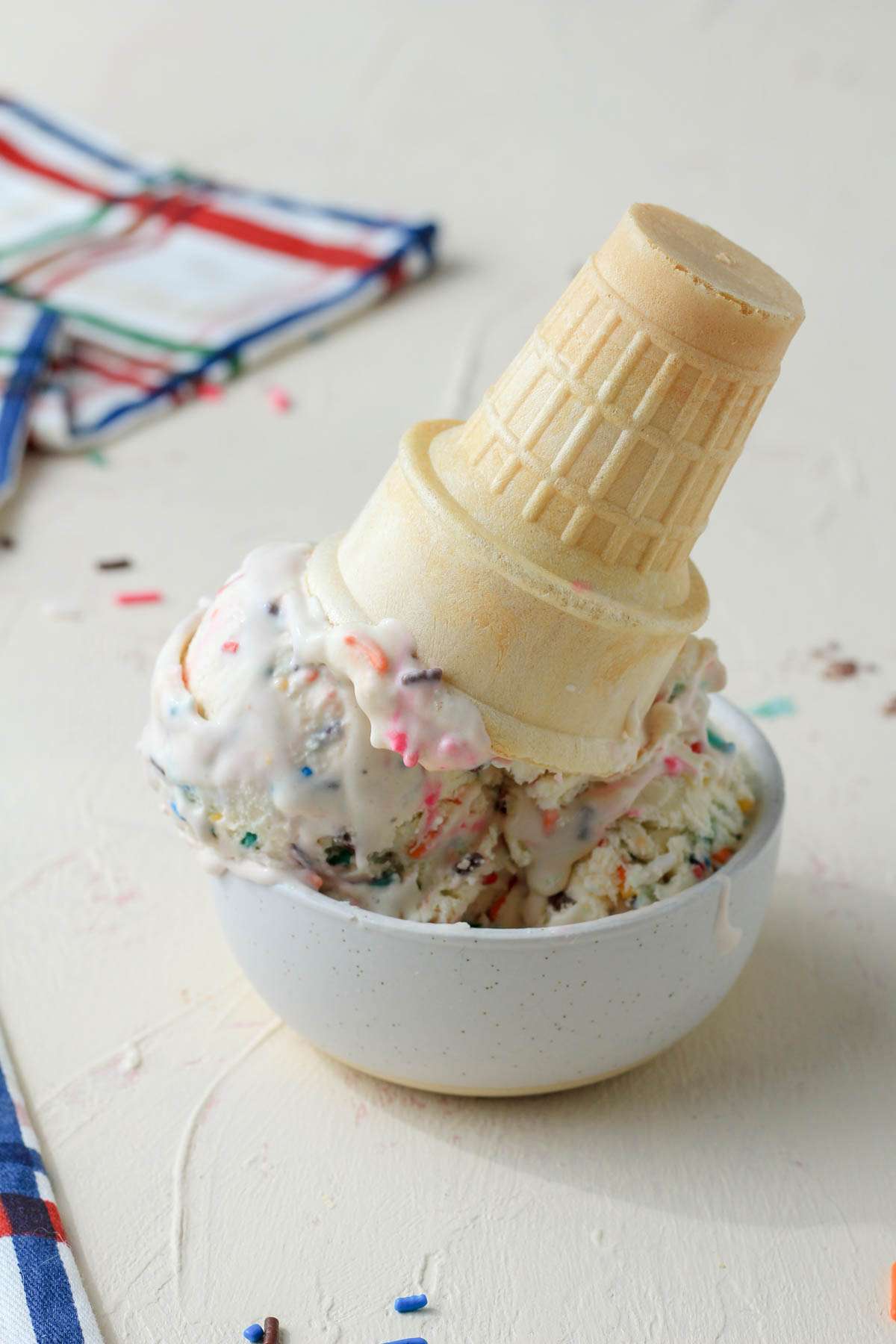 A small white bowl with scoops of dairy-free cake batter ice cream and an upside down ice cream cone in the bowl.