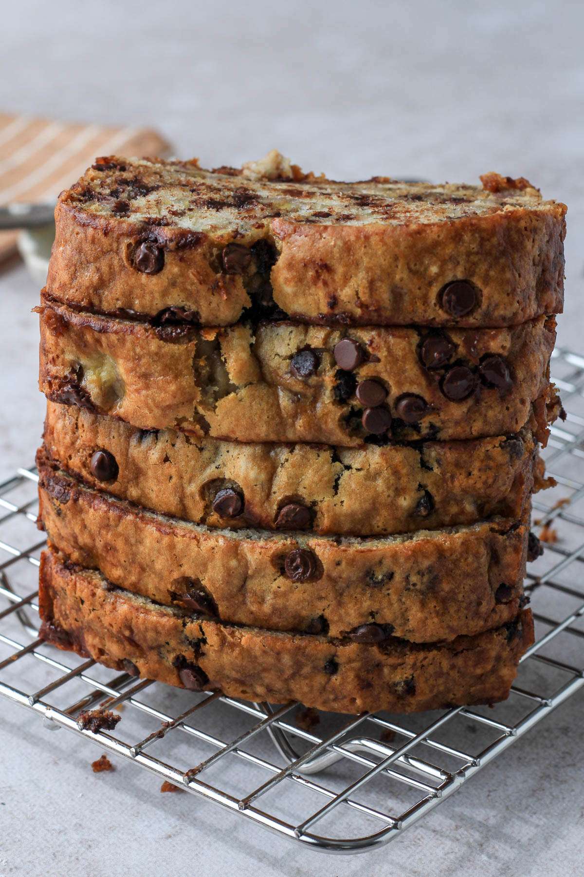 A wire cooling rack with a stack of five slices of vegan chocolate chip banana bread stacked vertically.