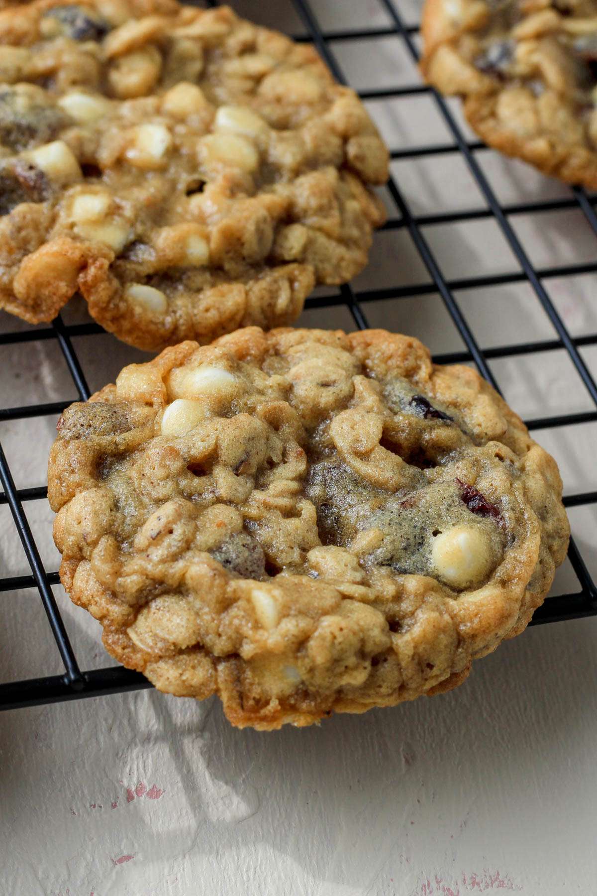 A black cooling rack on a cream counter with white chocolate craisin cookies from the side.