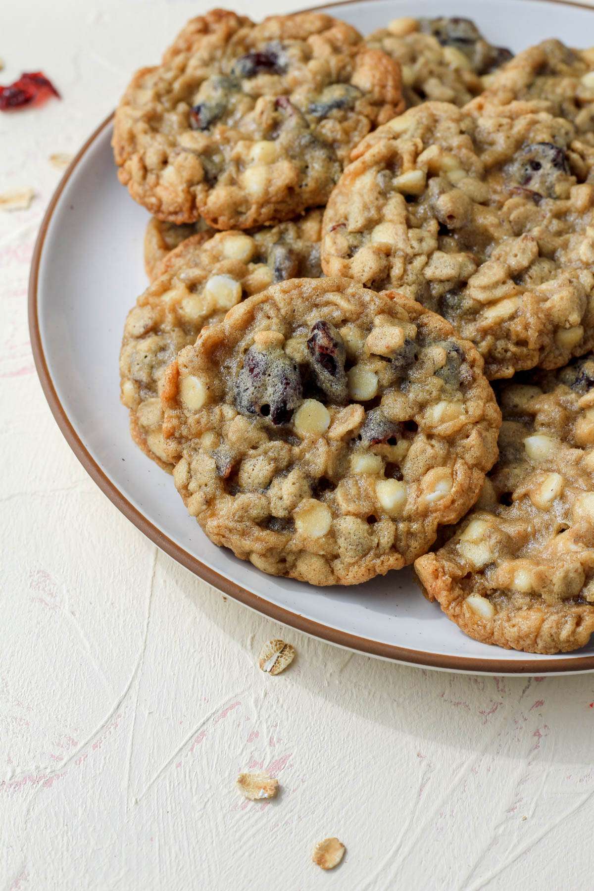 A white plate with a brown rim and a small stack of craisin and white chocolate chip oatmeal cookies on a cream counter.