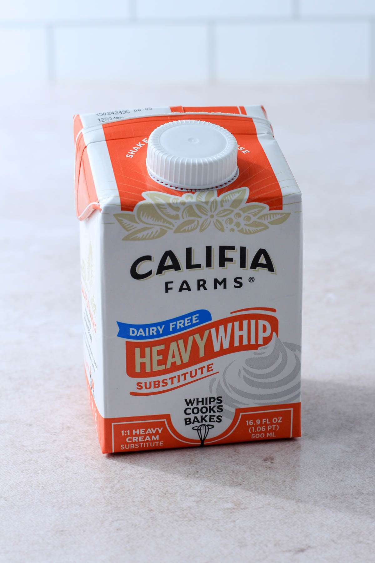 An orange and white carton of Califia Farms Dairy-Free Heavy Whip Substitute on a tan counter with a white background.