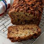 A loaf of cinnamon apple banana bread on a silver cooling rack with one slice cut off in the front.