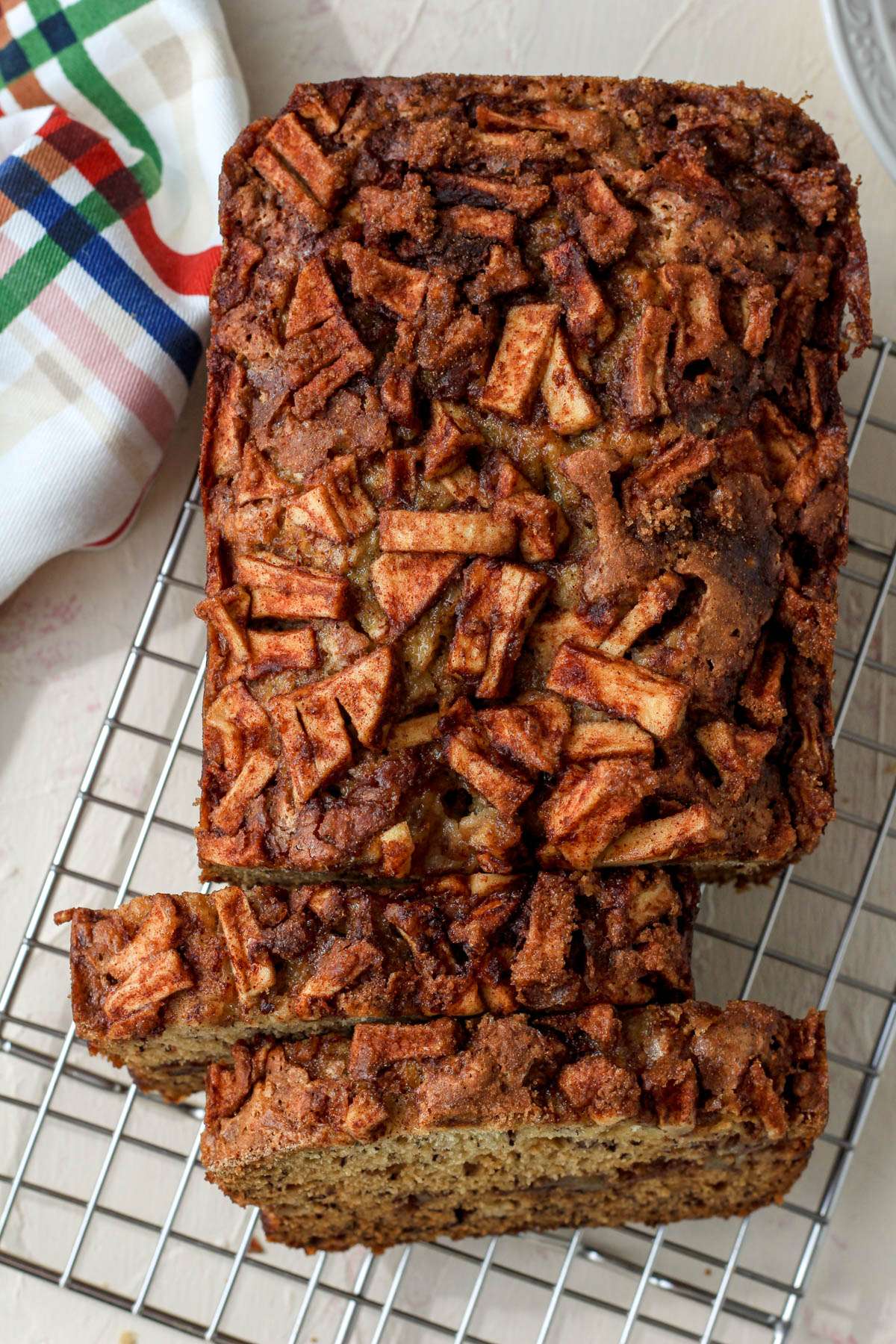 A top down image of a loaf of cinnamon apple banana bread on a cooling rack cut into 1 inch thick slices.