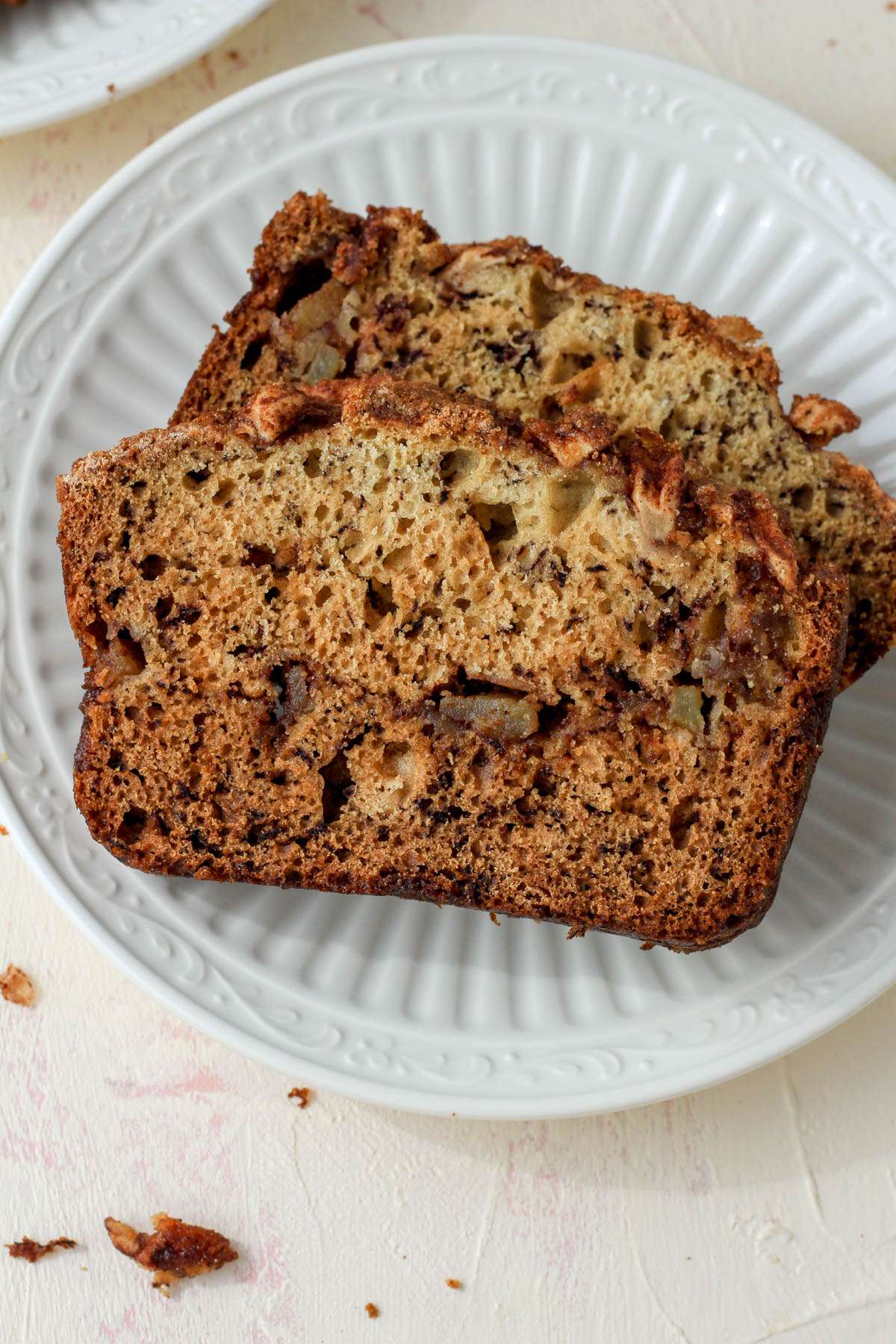 A white plate on a cream counter with two slices of dairy-free banana bread topped with cinnamon apples.