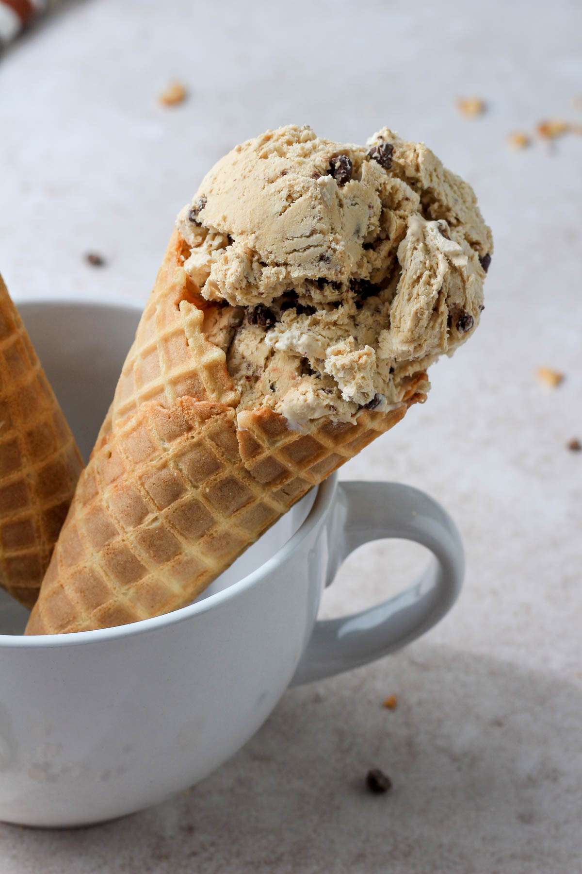 A white coffee mug with an ice cream cone filled with vegan coffee chip ice cream on a tan counter.