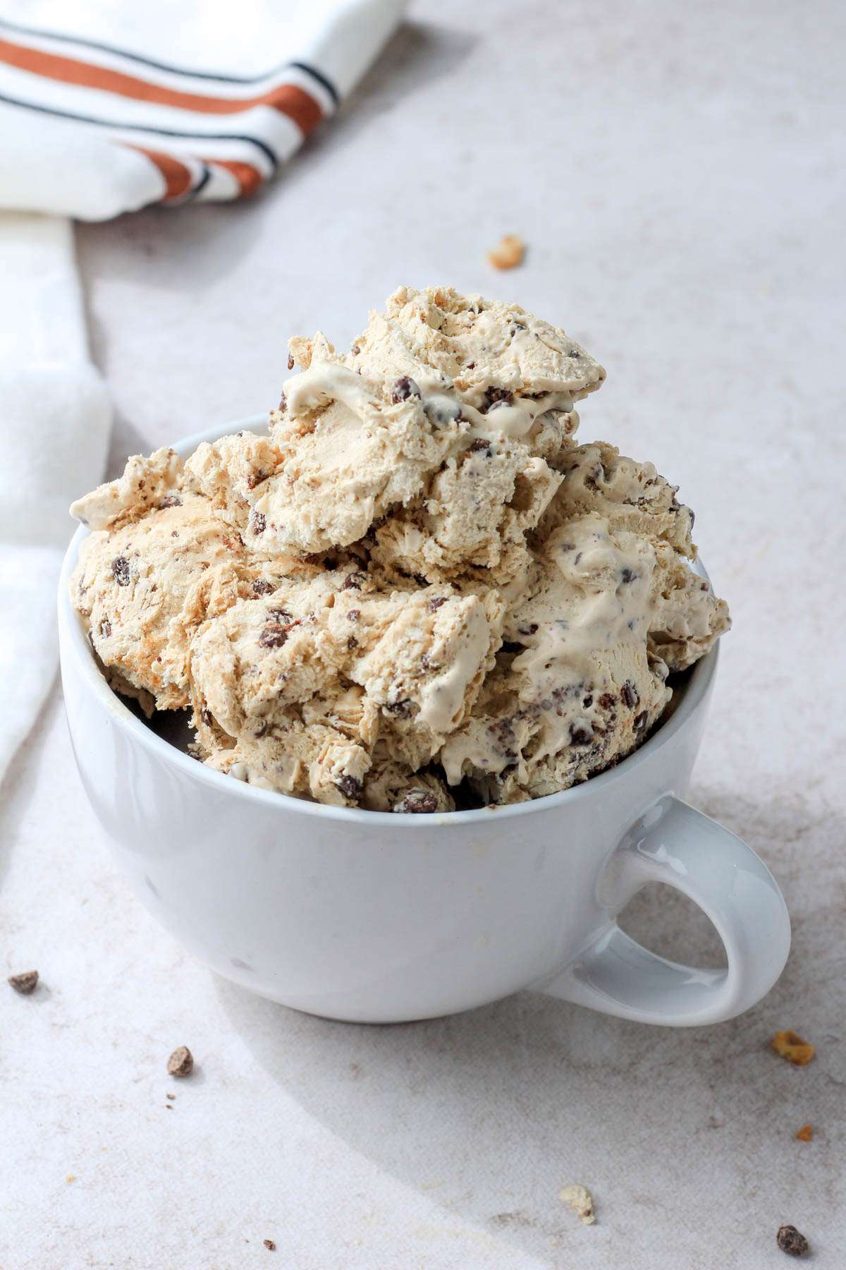 A white coffee mug overflowing with vegan coffee chip no churn ice cream on a tan counter.