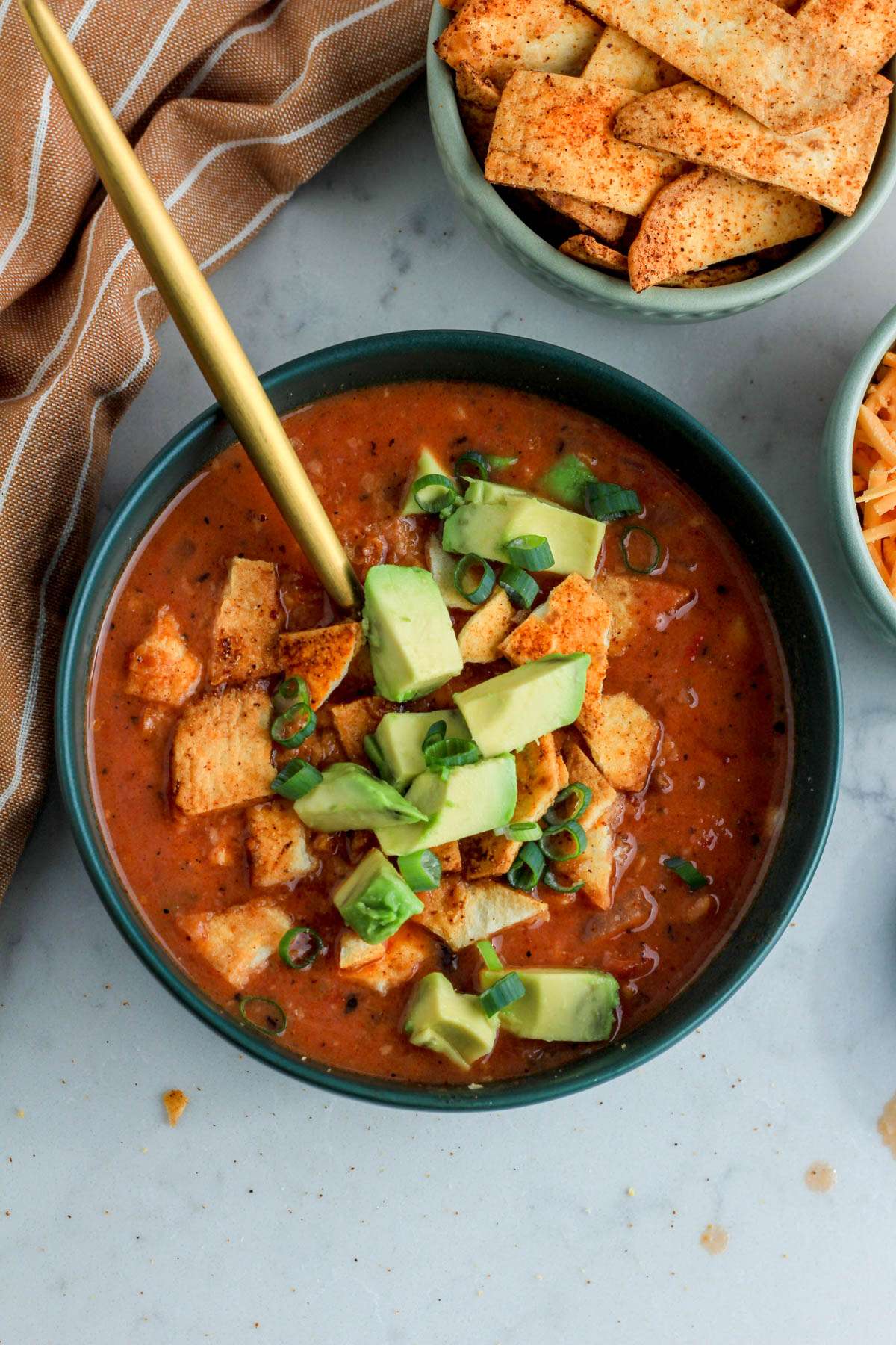 A green bowl with southwest chicken tortilla soup topped with tortilla strips, green onion, and avocado.
