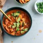 A cropped in image of a dark green bowl of creamy southwest chicken tortilla soup topped with tortilla strips and avocado chunks.