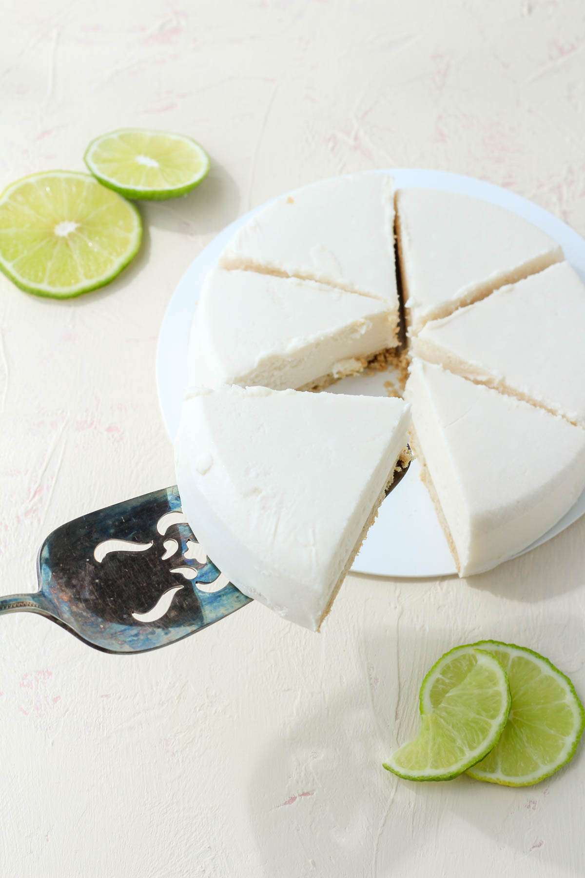 A silver pie server holding up a slice of the key lime cheezecake set aside from the other slices of key lime cheezecake.
