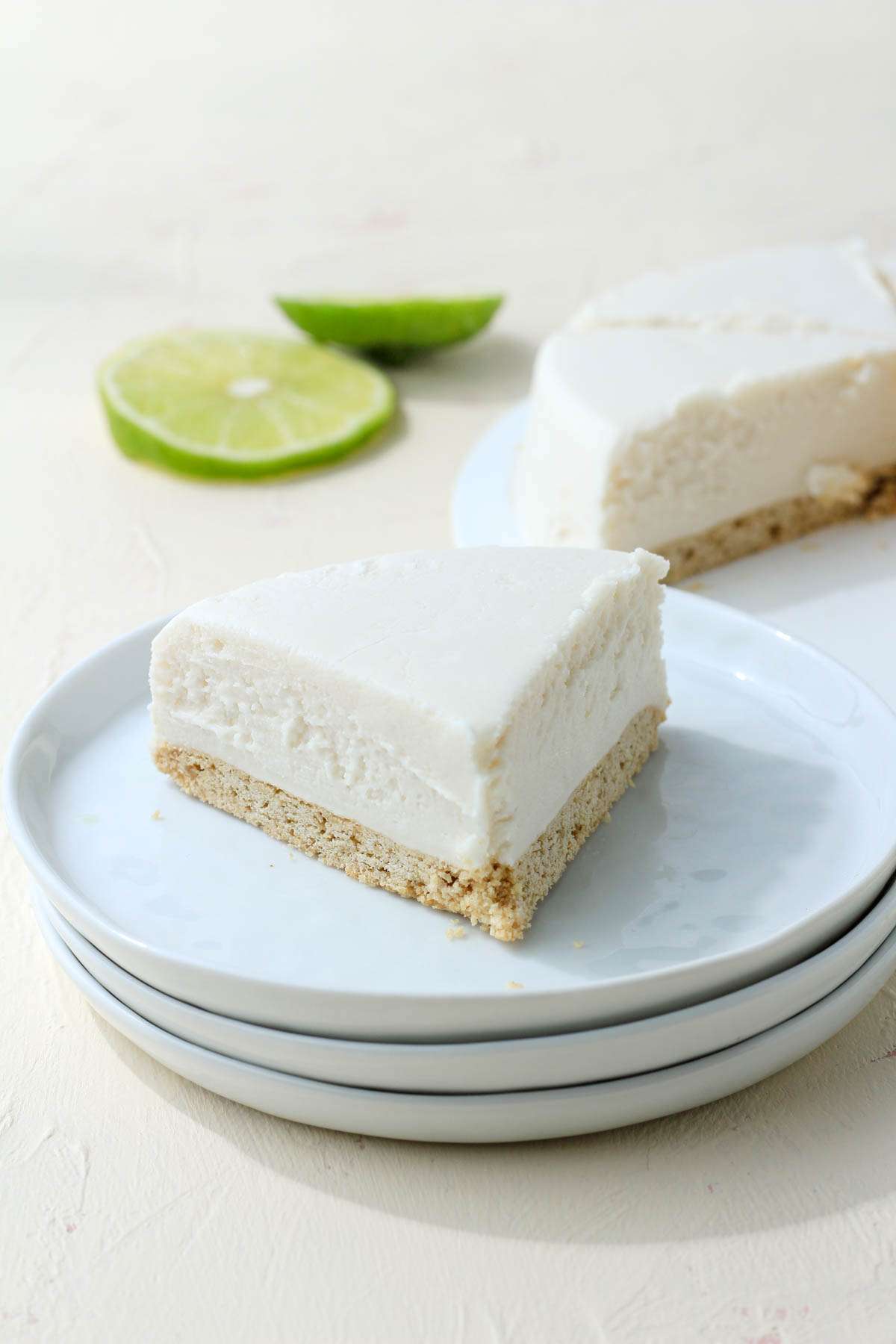 Stacked white plates with a slice of Daiya Cheezecake on top of the plates and some slices of lime in the back left.