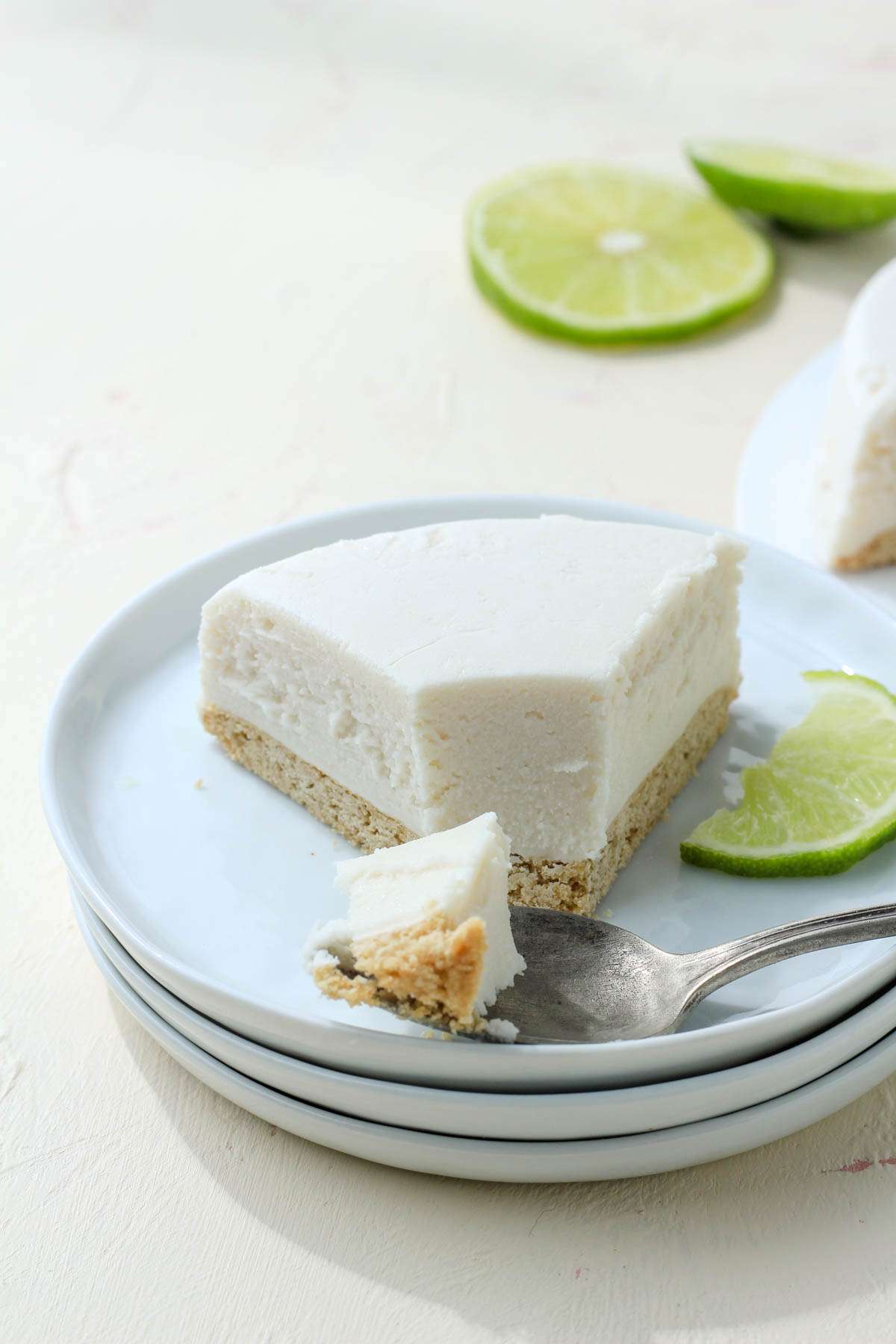 A small stack of white plates with a slice of Daiya cheezecake on the top plate with a silver spoon and a bite on the spoon.