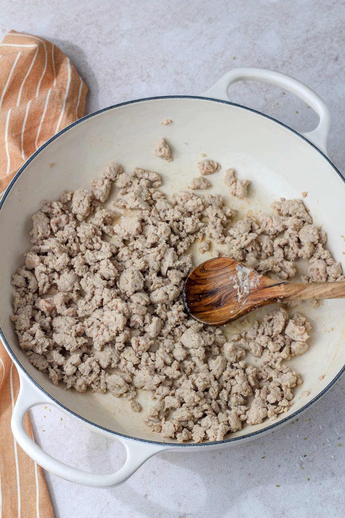A white pan with a wooden spoon and cooked ground turkey.
