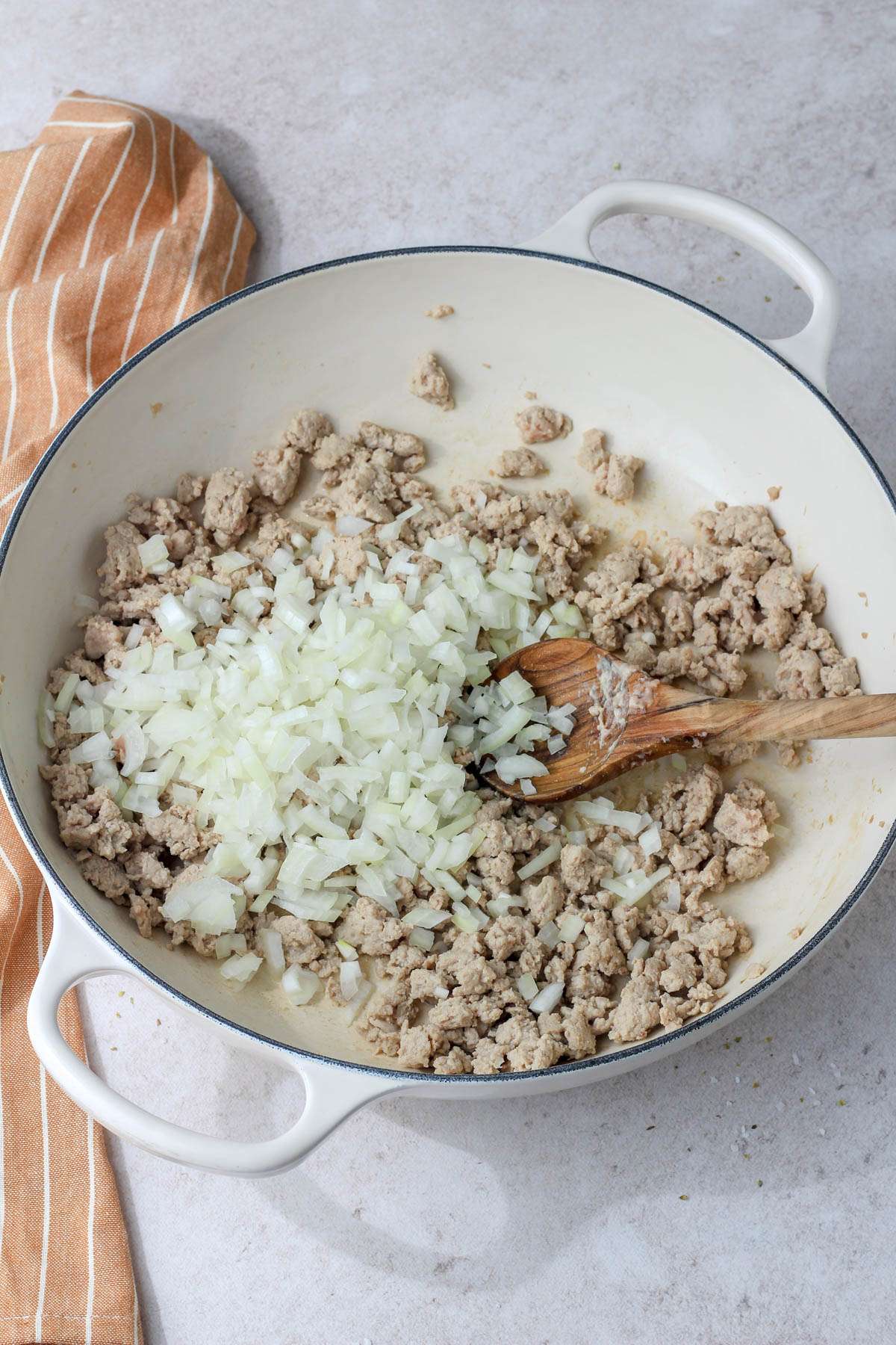 A white pan with a wooden spoon and cooked ground turkey with onion.