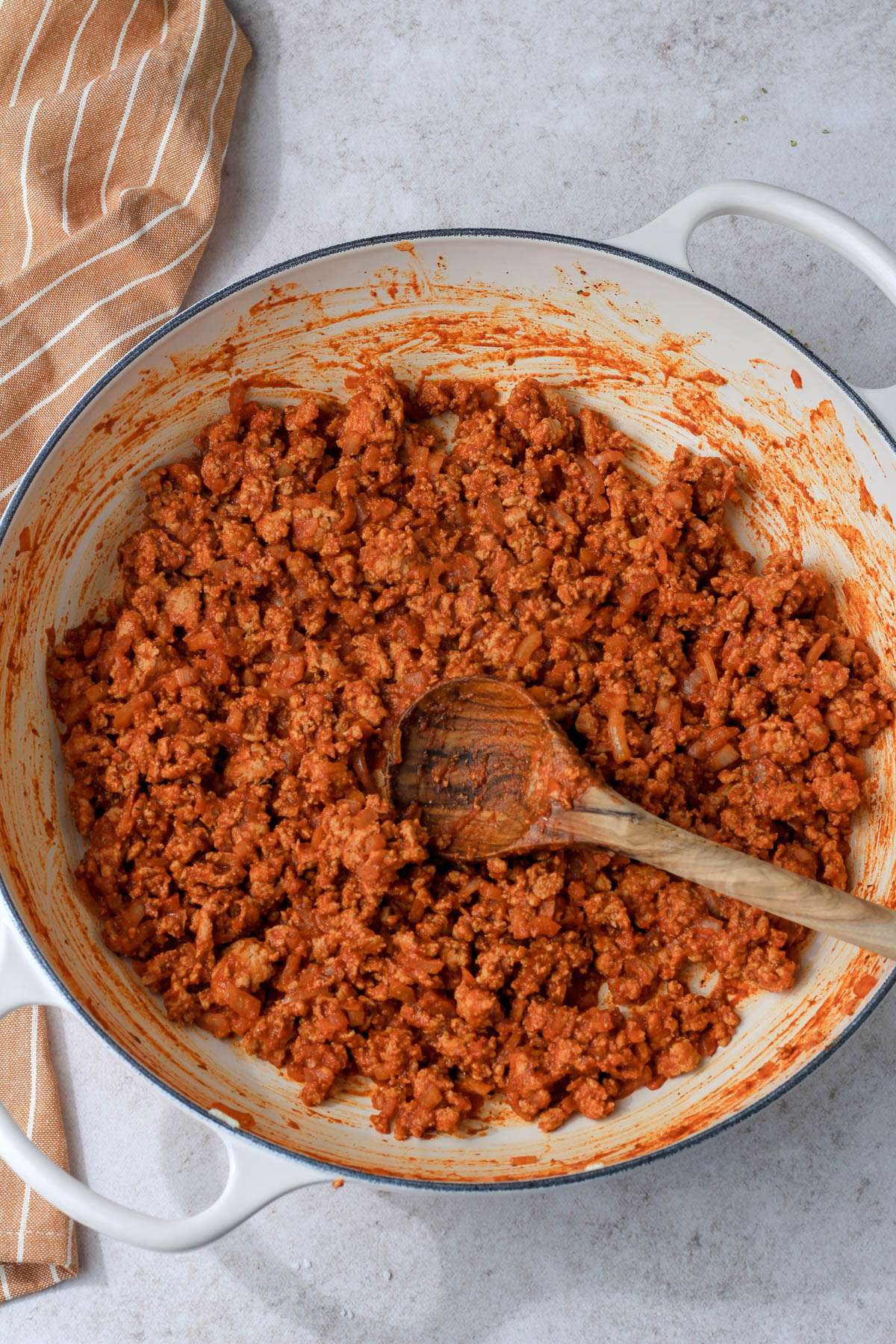 A white skillet with a wooden spoon and ground turkey taco meat.