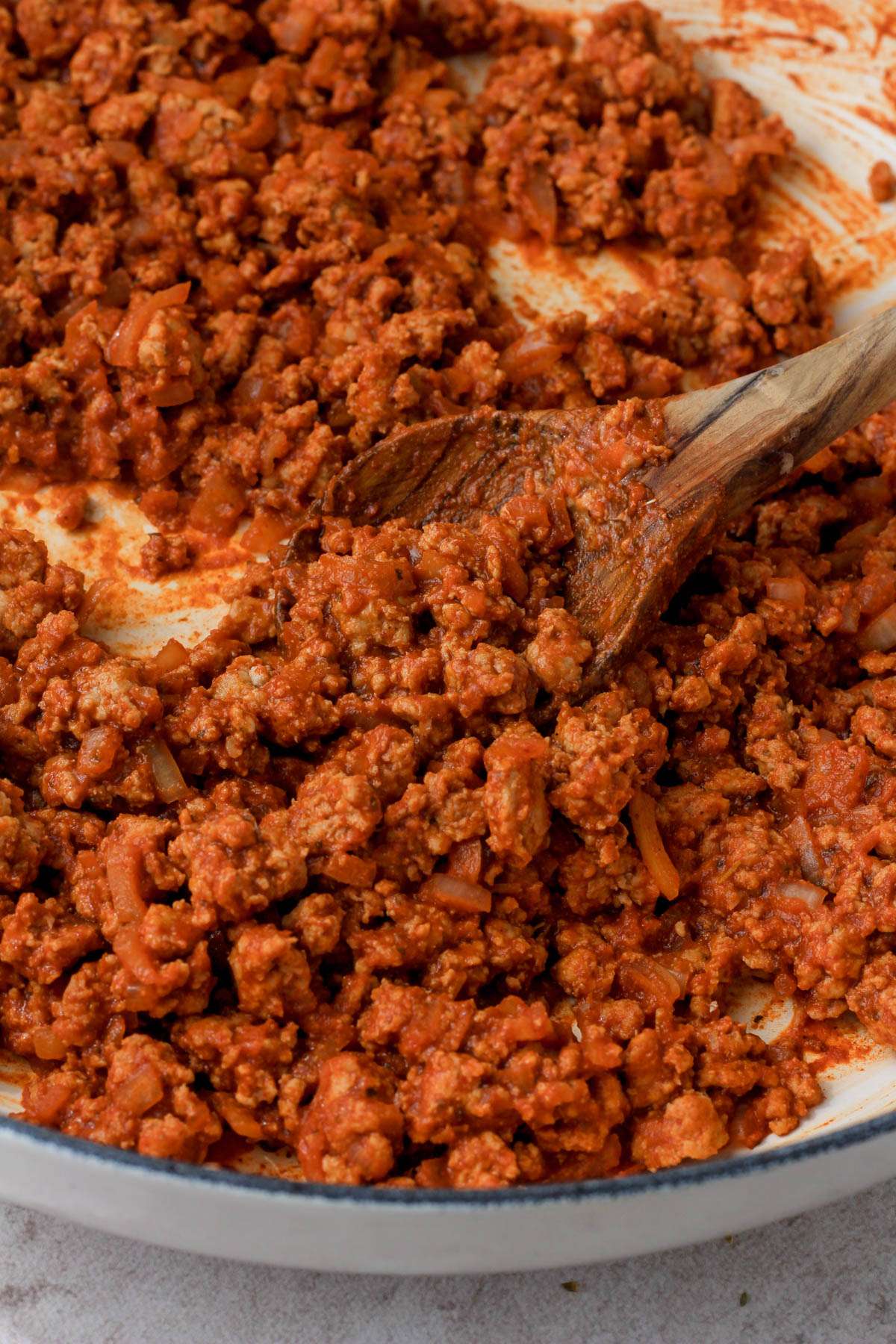 From the side, a white skillet with ground turkey taco meat being scooped by a wooden spoon.