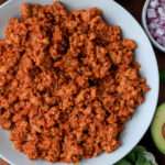 A close up of a white bowl on a wooden counter with ground turkey taco meat.