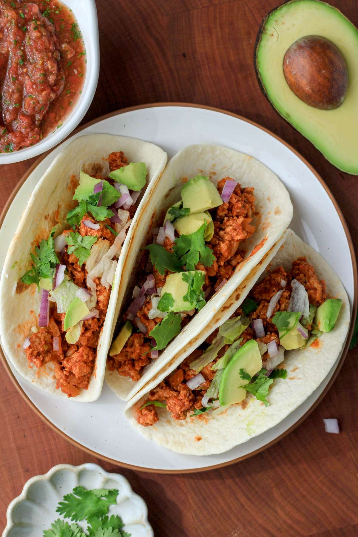 A small white plate with a brown rim topped with three turkey tacos on a wooden cutting board.