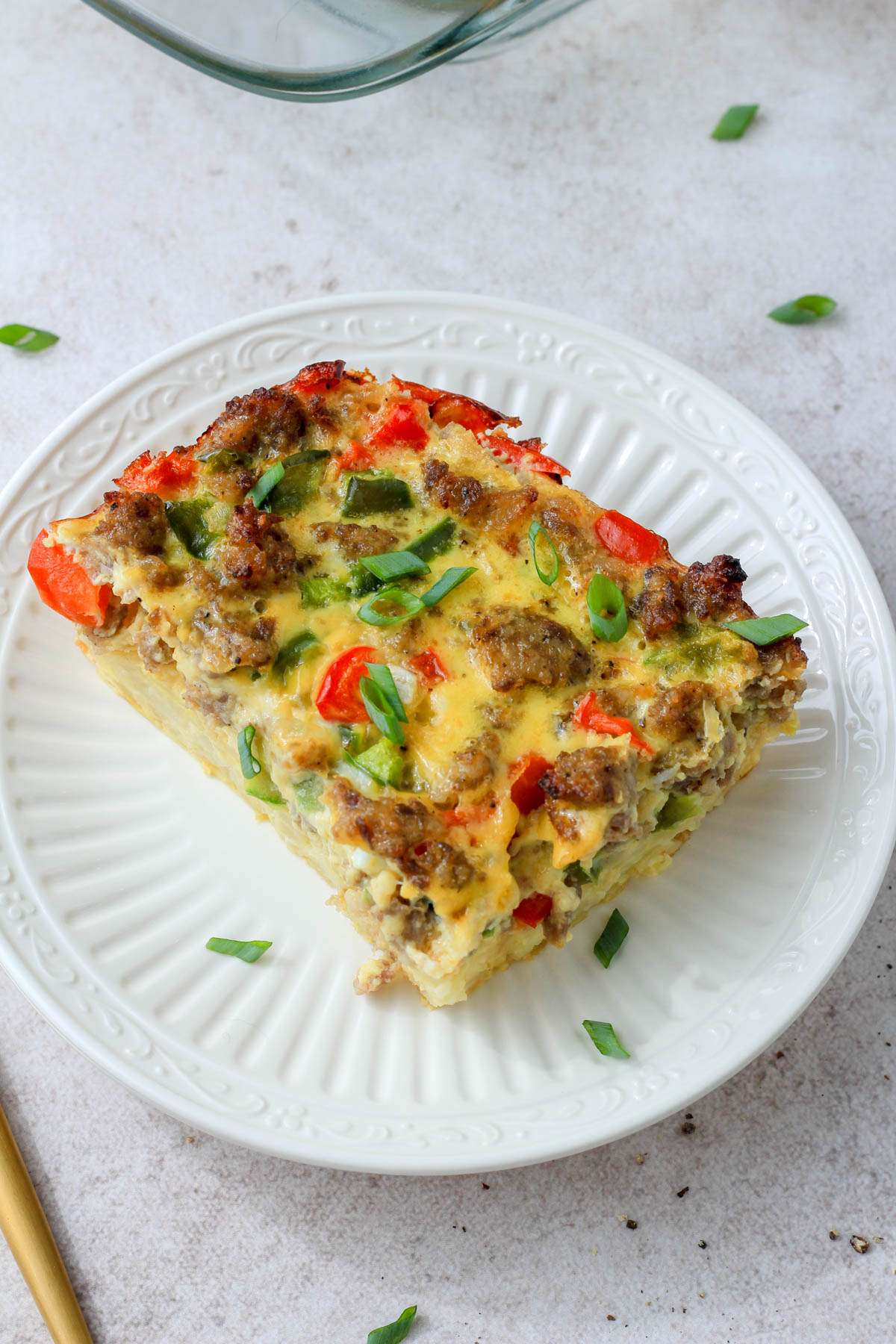 A small white plate with a slice of hashbrown casserole with a gold fork on the left side.
