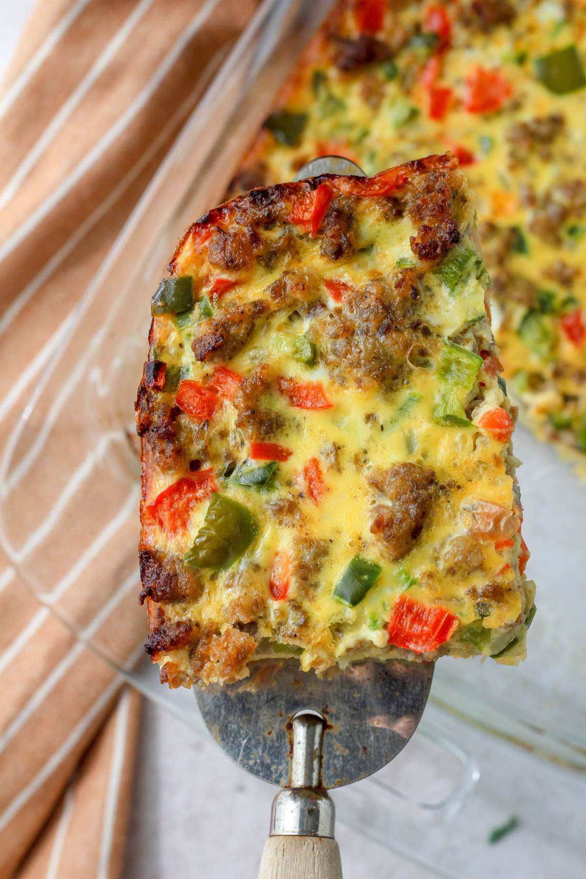 A silver server lifting a slice of hashbrown casserole out of a glass baking dish.