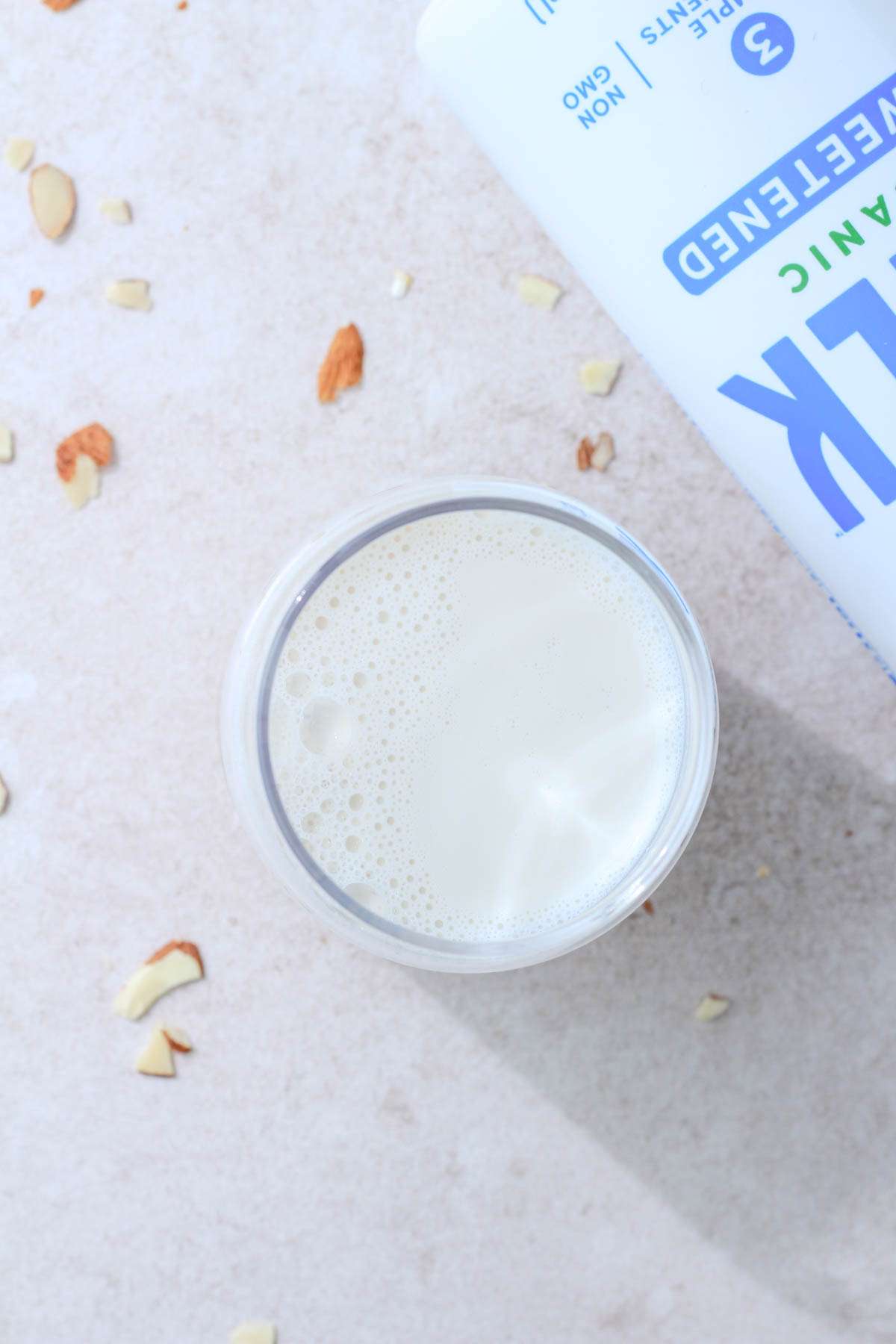 A top down image of a glass of almond Malk next to a bottle of malk laying on the counter.