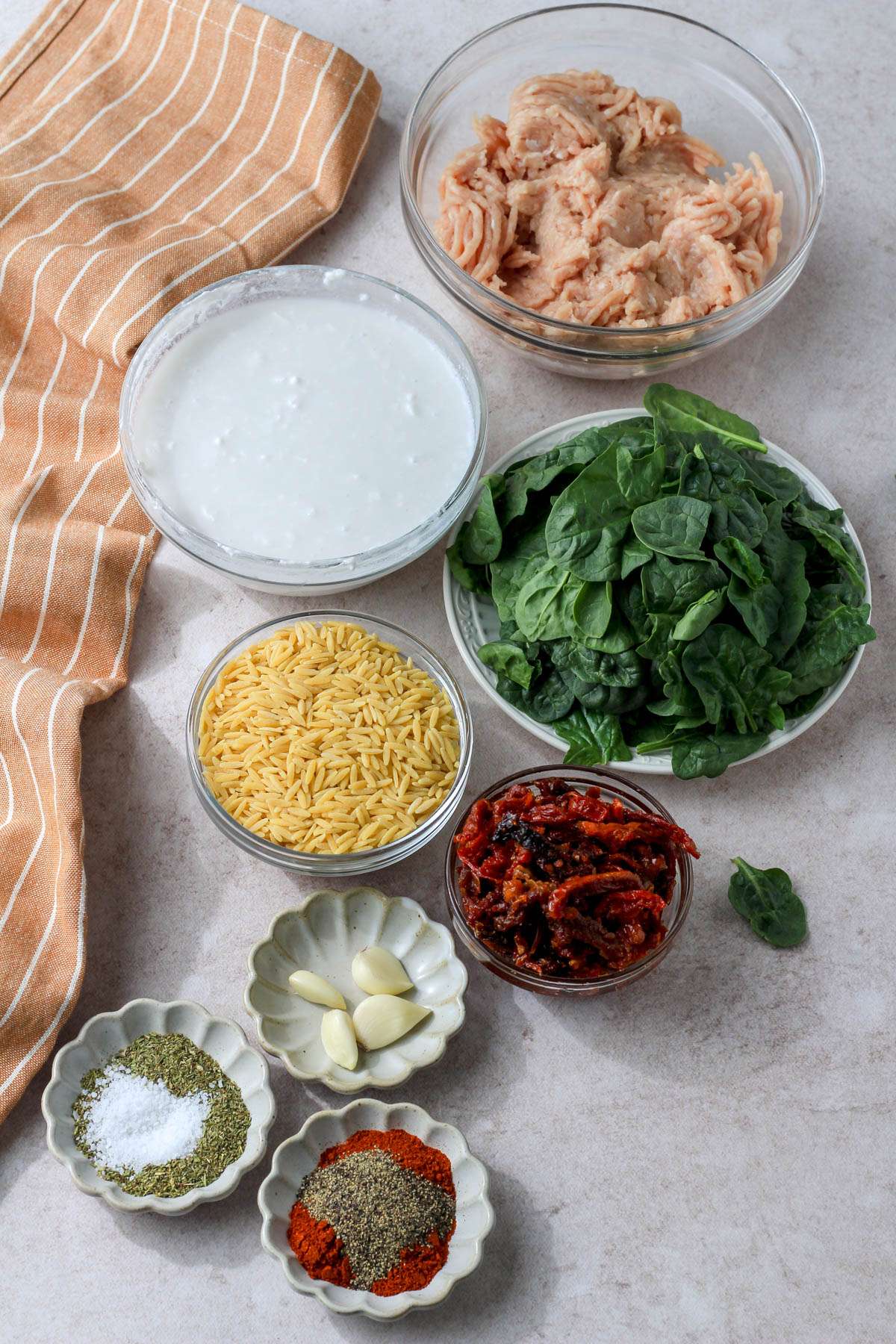 Ingredients for dairy-free marry me ground chicken and orzo on a tan counter.