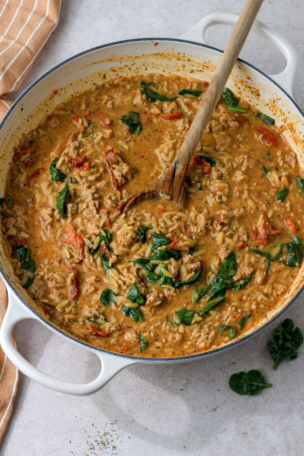 A white skillet with a wooden spoon and cooked marry me ground chicken and orzo on a tan counter.