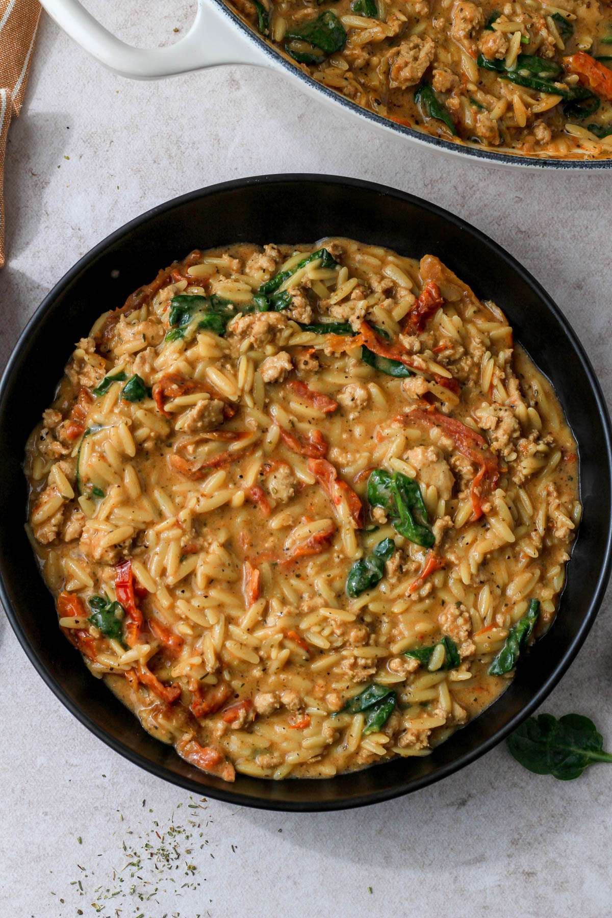 A black bowl filled with dairy-free marry me ground chicken and orzo on a tan counter.