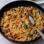 A black bowl with a large silver spoon scooping dairy-free marry me ground chicken and orzo pasta.
