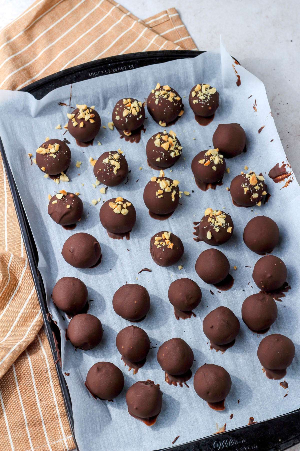 A parchment paper lined baking sheet with peanut butter oreo truffle balls after being dipped and topped with crushed peanuts.
