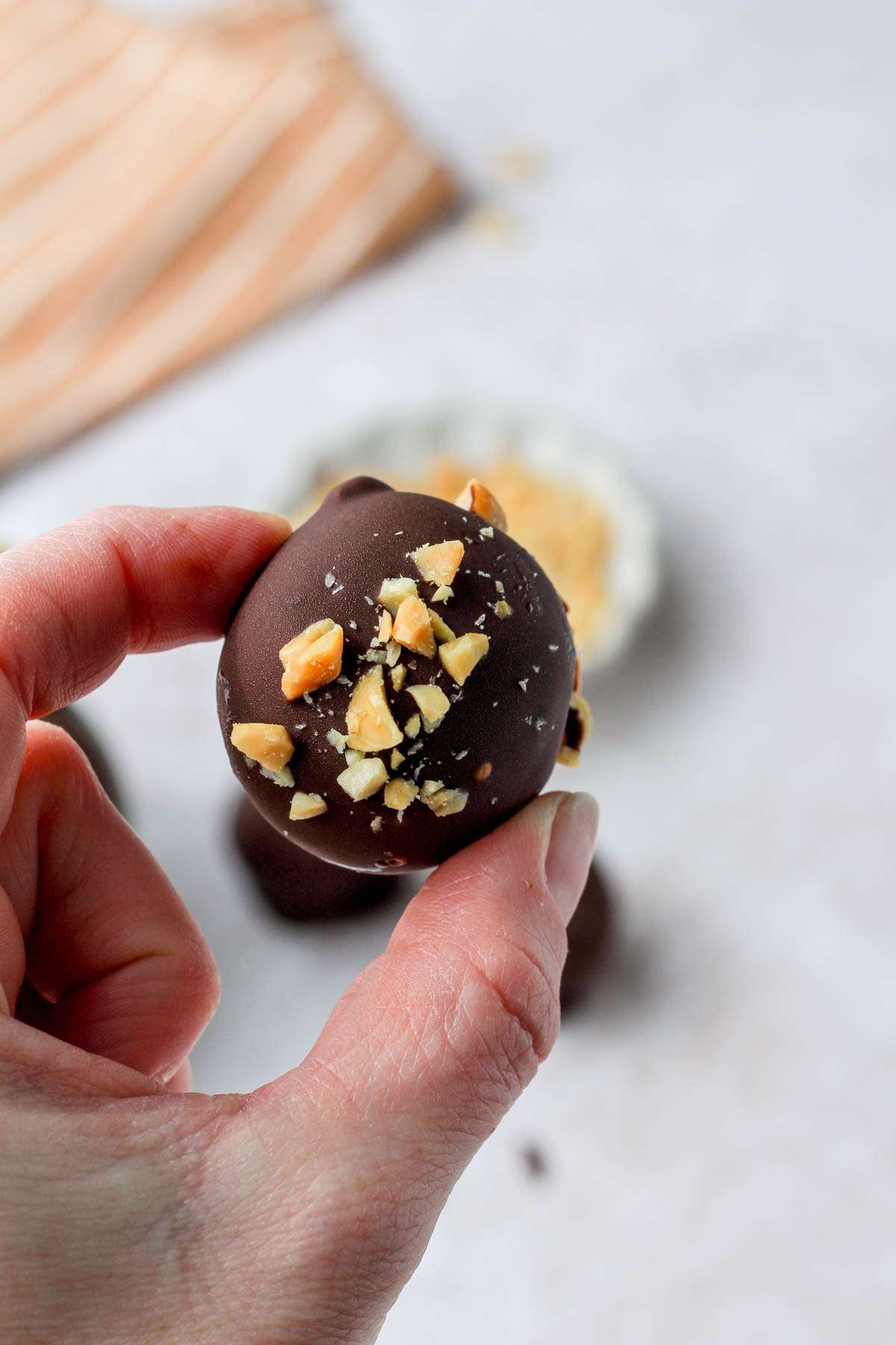 A hand holding a peanut butter oreo truffle topped with crushed salted peanuts.