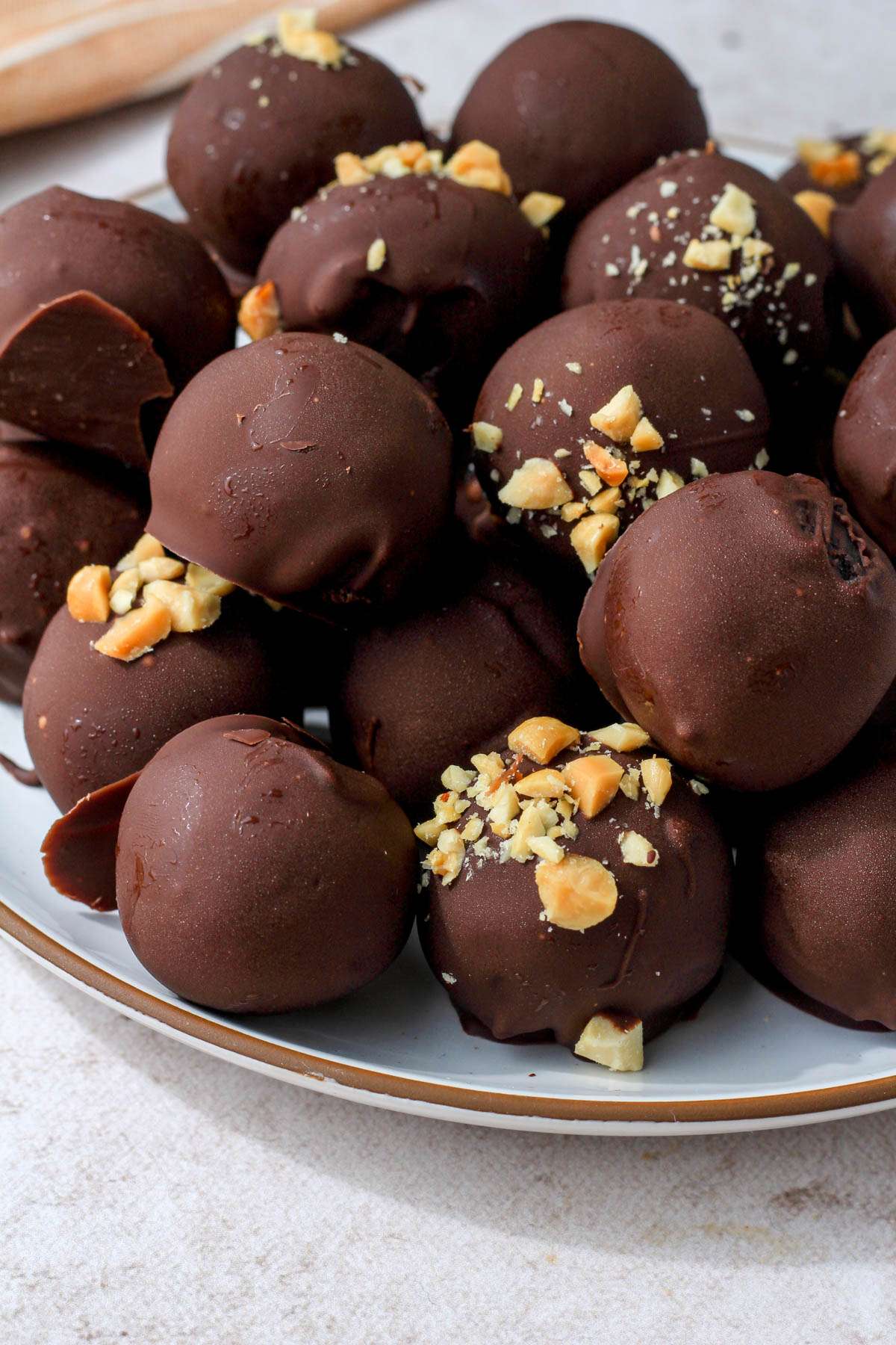 A white plate with a brown rim topped with a pile of chocolate peanut butter oreo truffles.