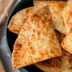 The green rim of a bowl filled with seasoned air fryer tortilla chips with one angled at the top.