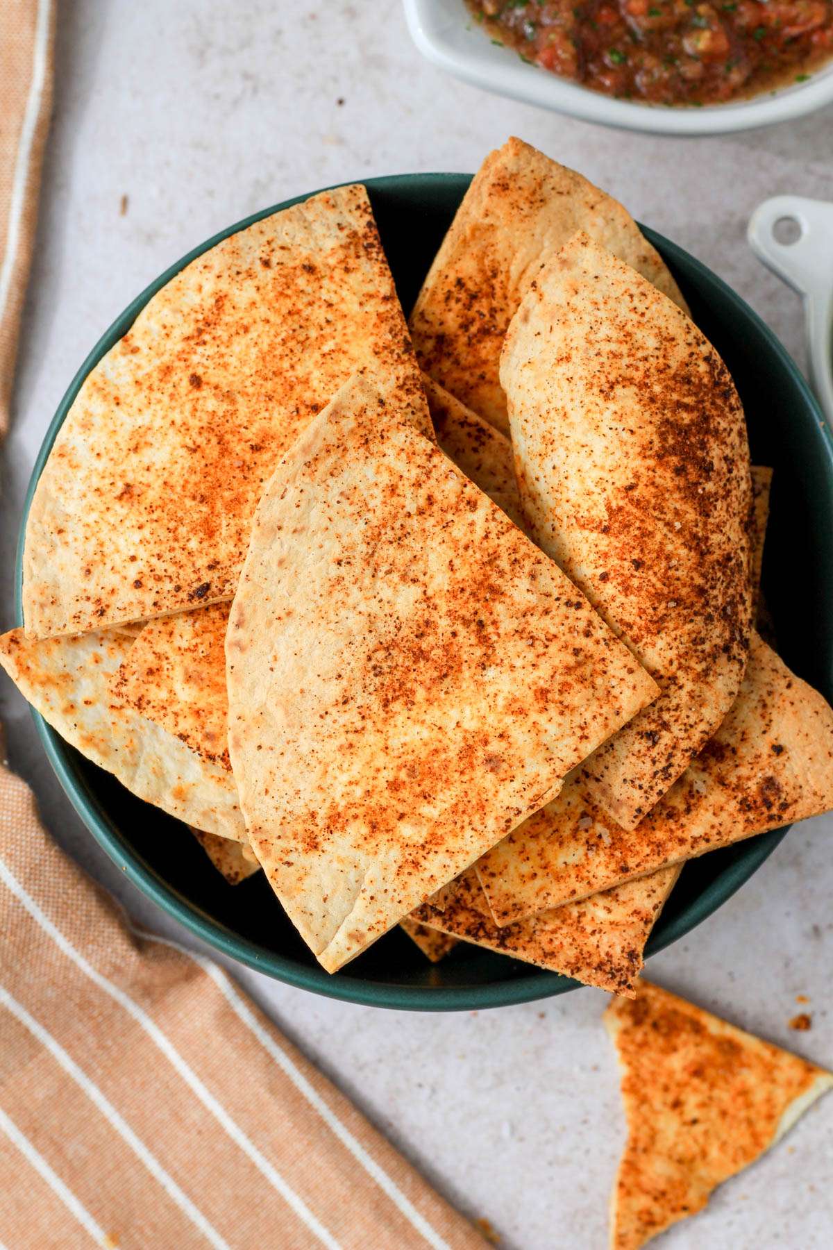 A green bowl on a tan counter with seasoned flour tortilla chips made in the air fryer.