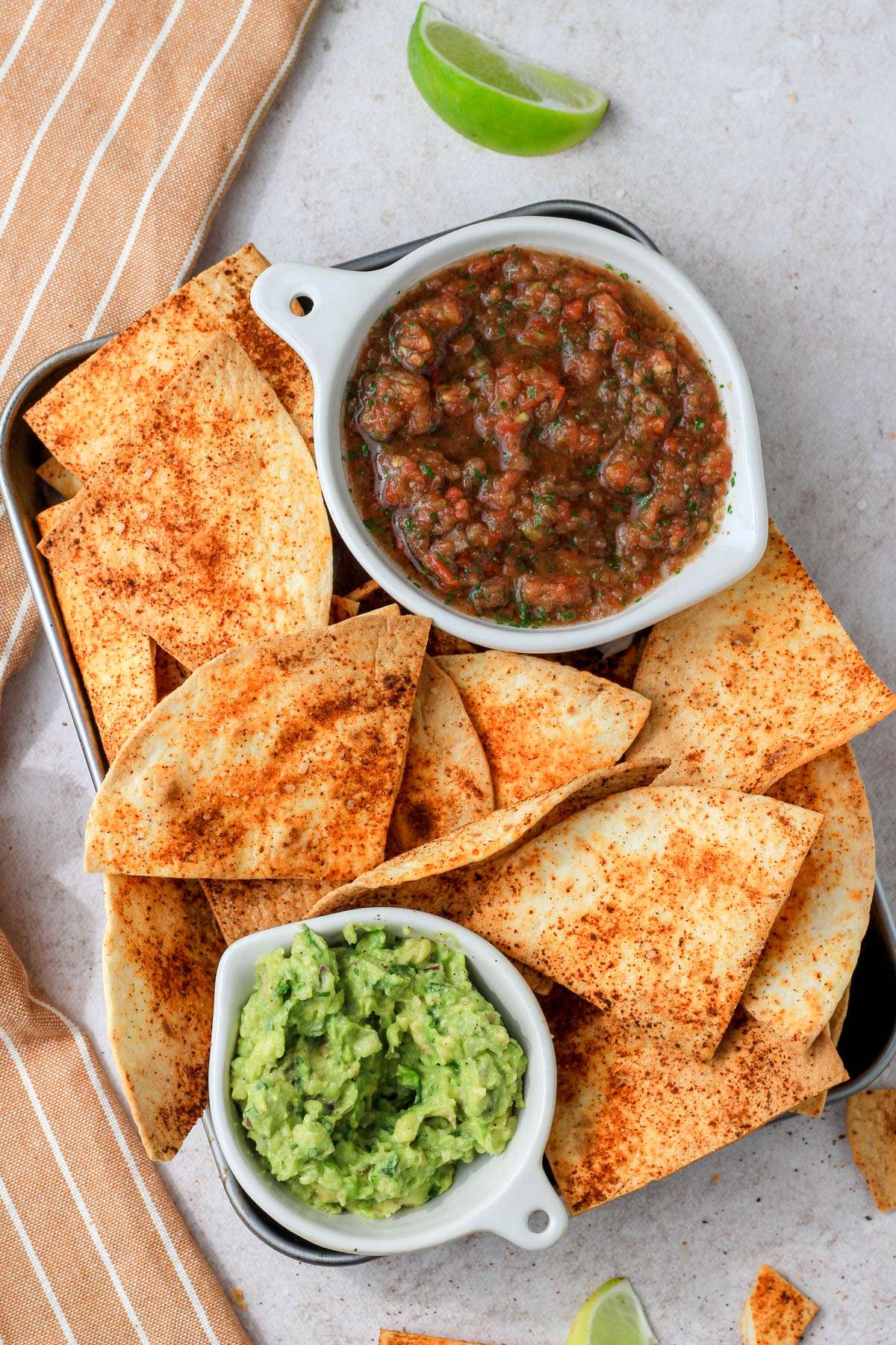 A silver pan filled with seasoned air fryer tortilla chips surrounding a small bowl of guacamole and salsa.