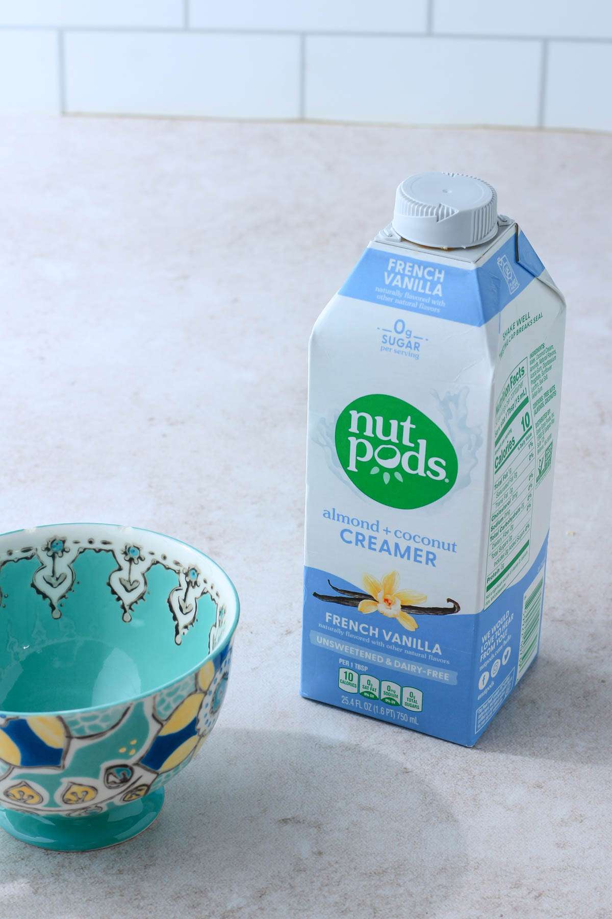 A blue and white carton of nut pods creamer on a tan counter by a blue coffee cup.
