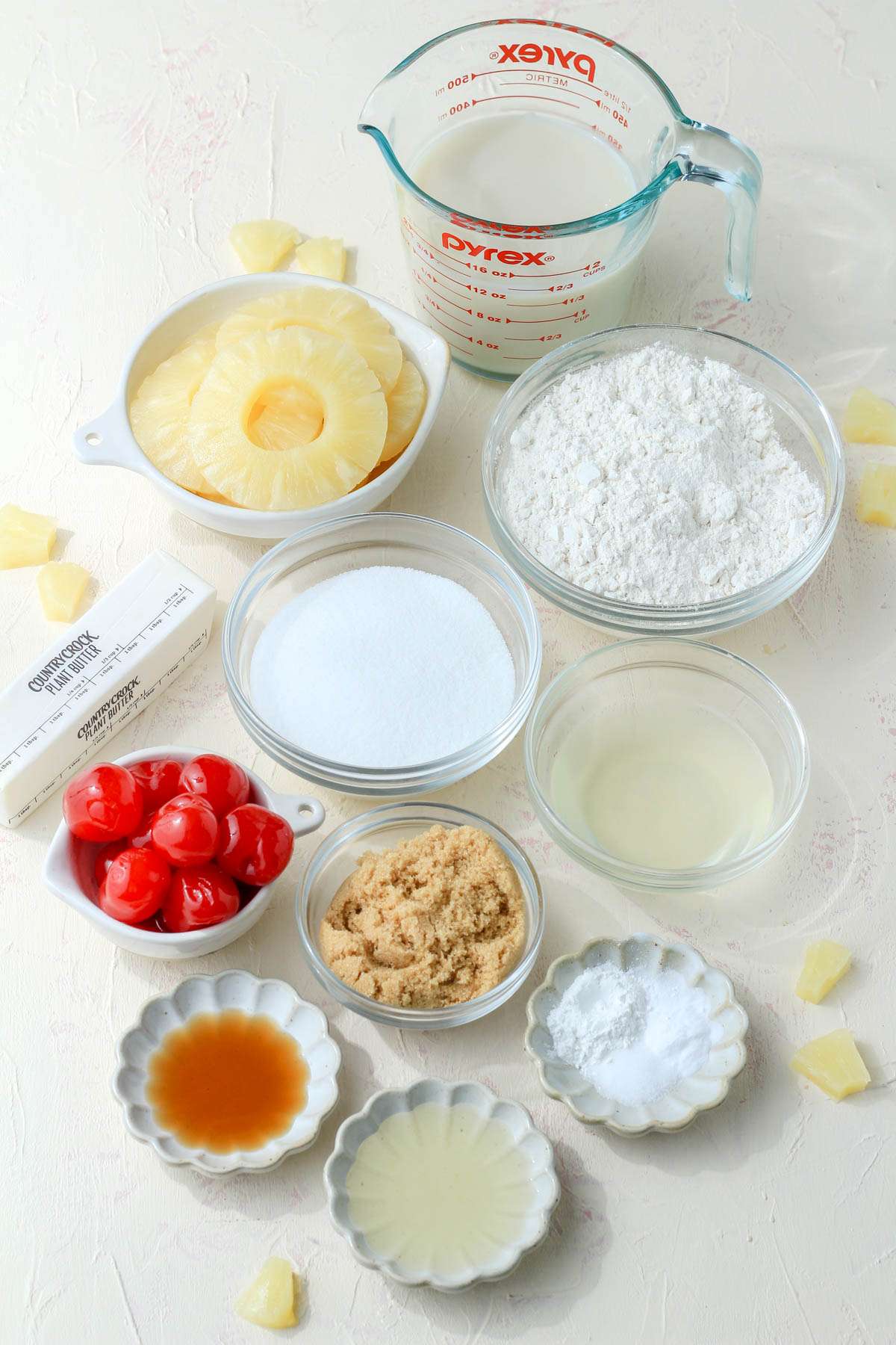 Ingredients for vegan pineapple upside down cake on a cream counter with chunks of pineapple around.