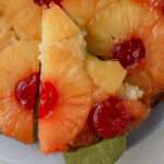 A close up of a slice of vegan pineapple upside down cake on a gold server.