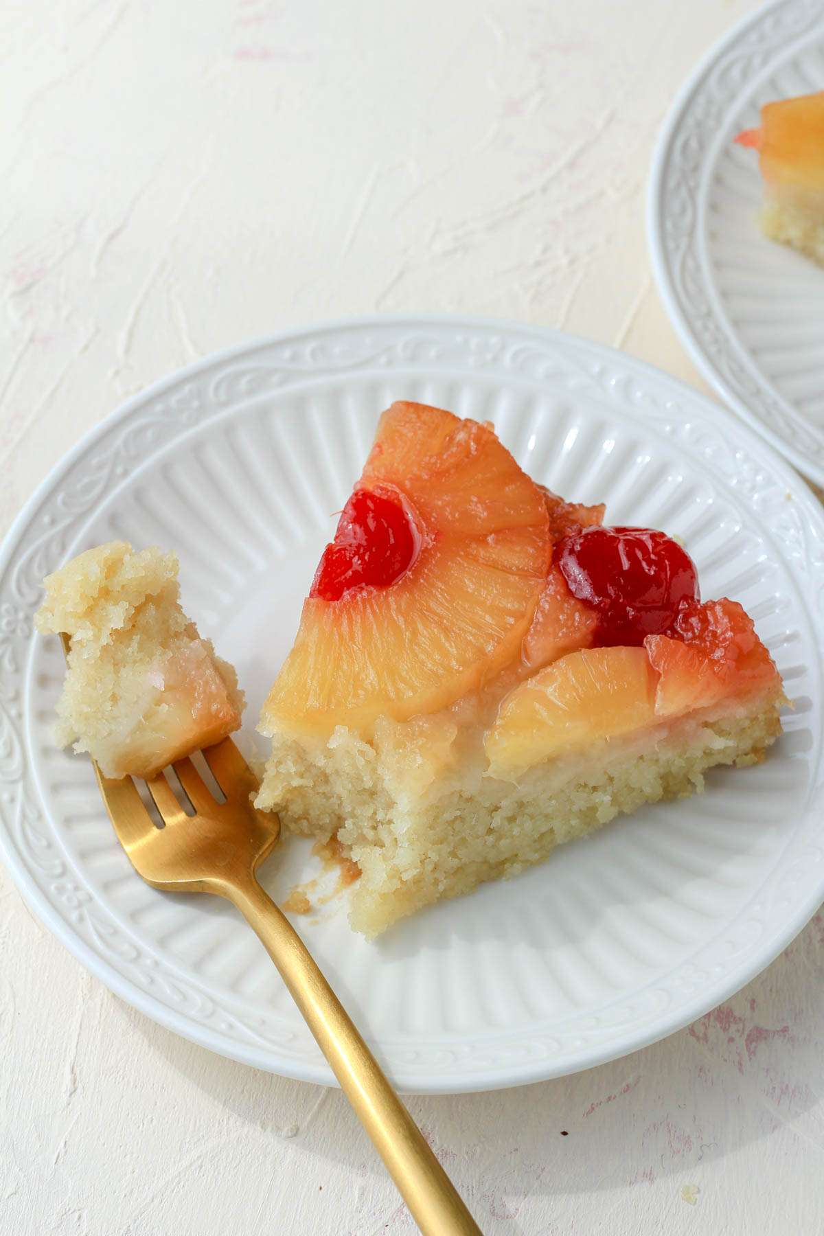 A top down angle of a slice of pineapple upside down cake with a bite take out on a gold fork in front of the slice.